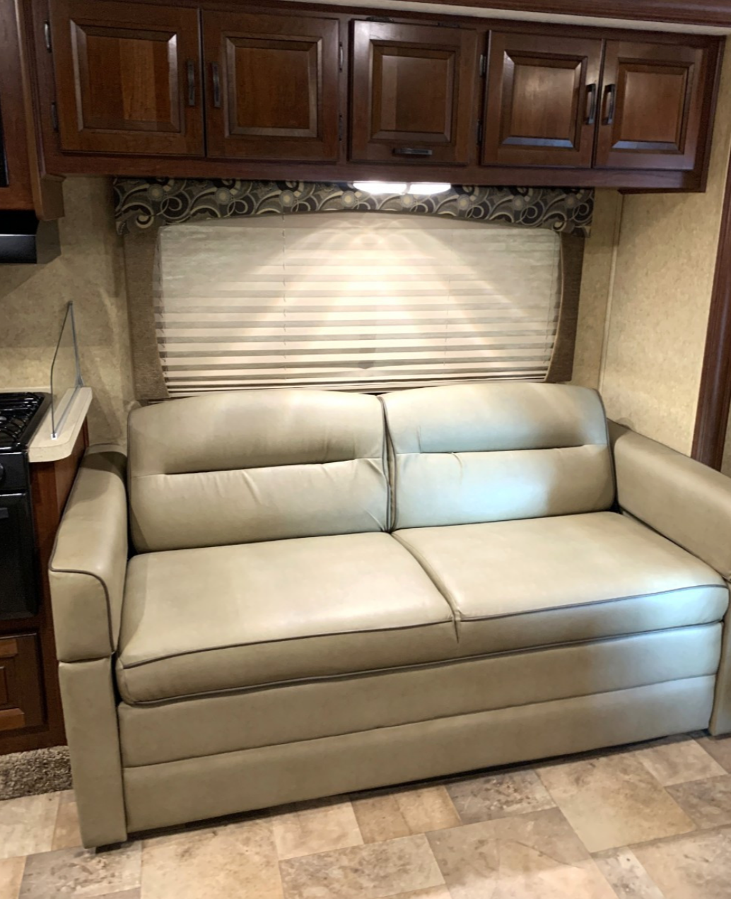 RV rental living area: cream sofa bed with dark piping, wooden cabinets, and window with blinds.. Forest River Sunseeker 2013