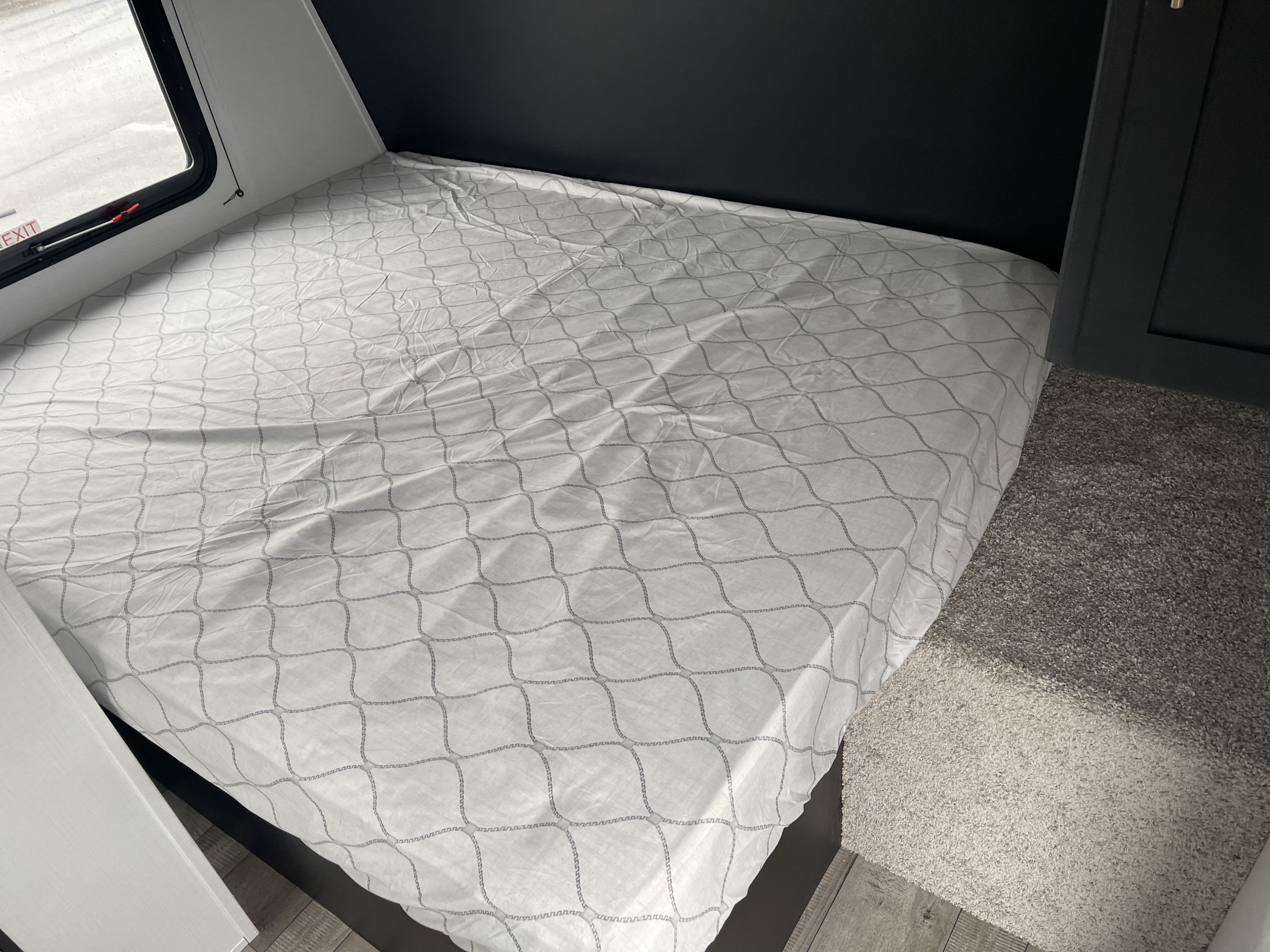 RV rental interior: A compact bed with a white patterned sheet, featuring a nearby window and dark built-in furnishings.. Keystone Springdale 1750 2022