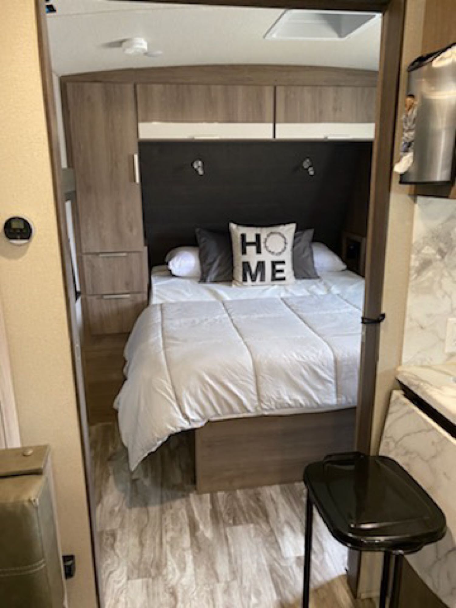 A welcoming RV rental bedroom with a cozy bed, "HOME" pillow, wood-grain cabinets, and modern flooring. Enjoy comfortable travel.. Grand Design Imagine 2021