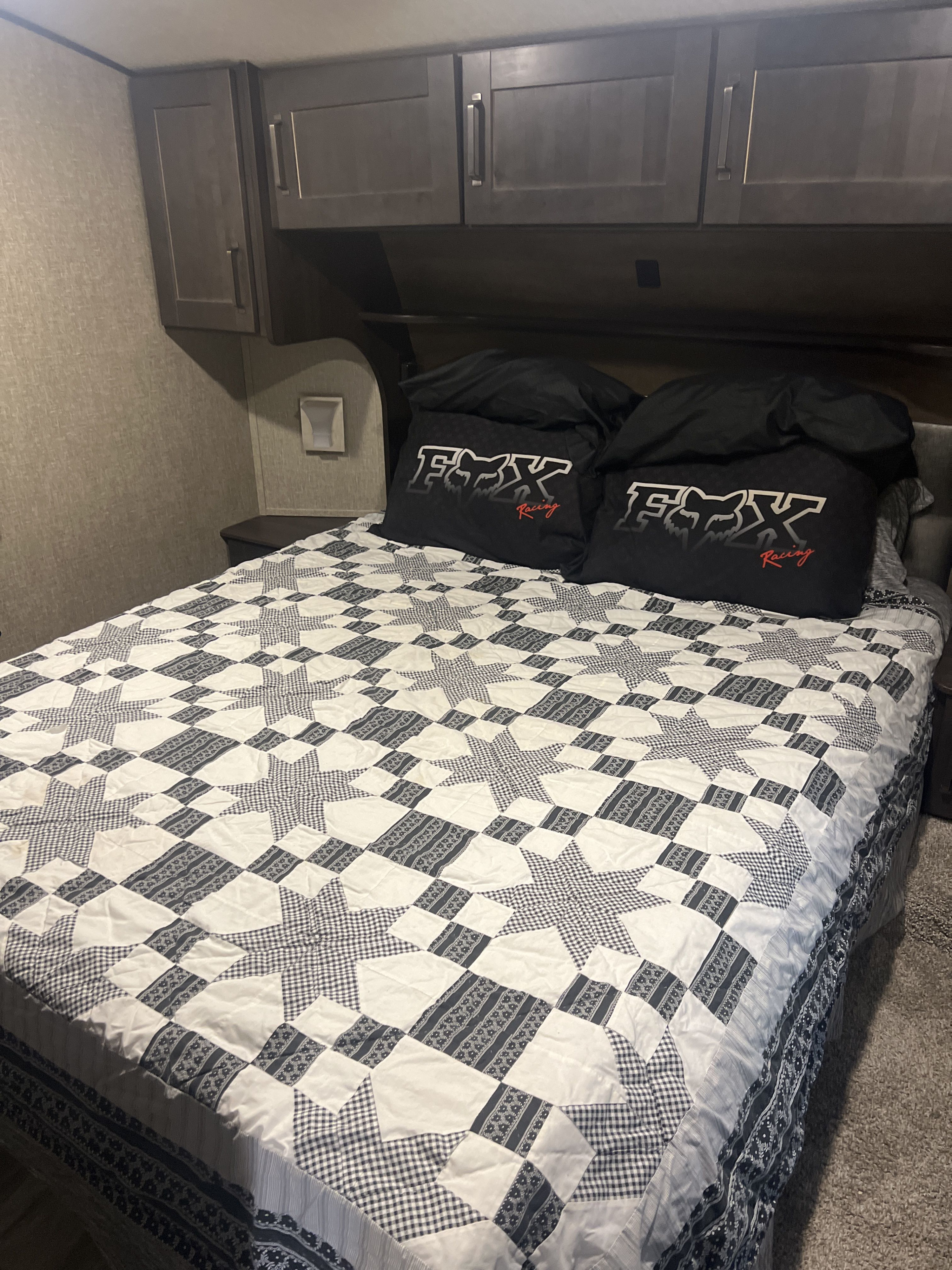 RV rental bedroom with a detailed black and white quilt, Fox Racing pillows, and overhead storage cabinets.. Grand Design Reflection 2021