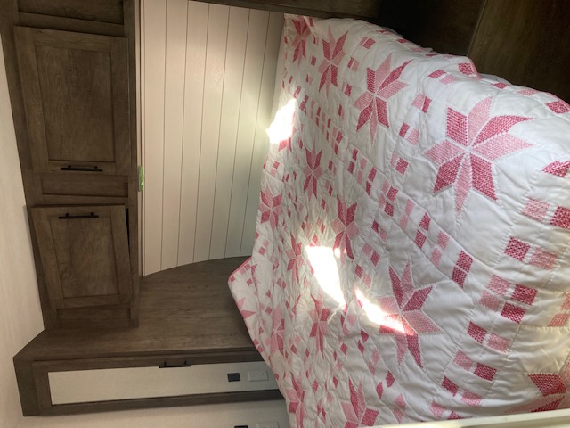 Compact RV rental bedroom showcasing a pink star quilt, wood storage, and white shiplap walls.. Forest River Salem 2020