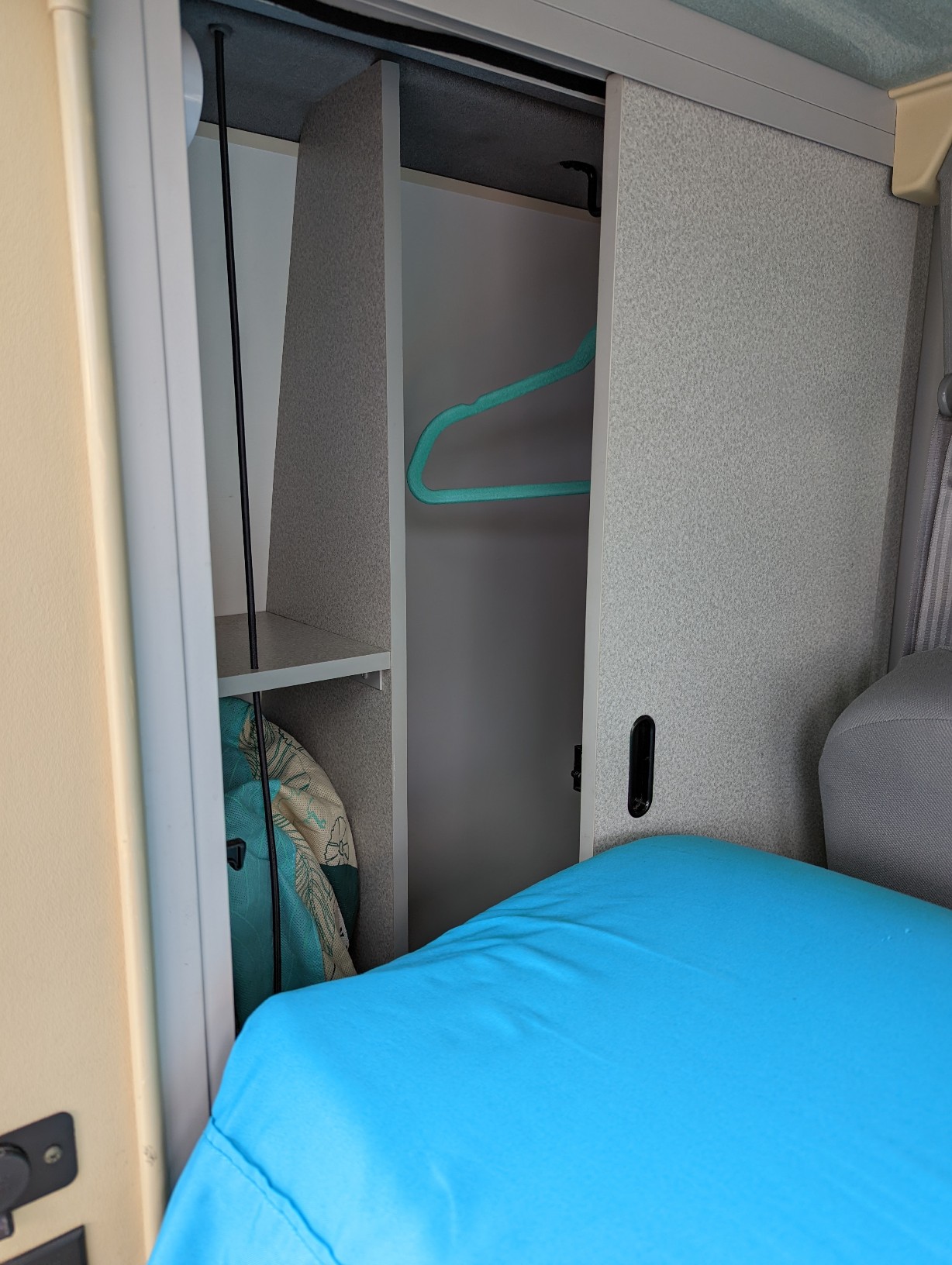 RV rental: Compact interior wardrobe with a turquoise hanger, lower shelf, and a vibrant blue bed.. Volkswagen Eurovan 2001