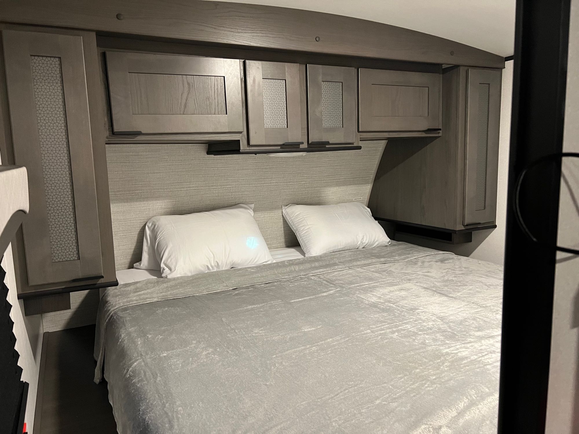 RV rental bedroom featuring a cozy bed with white pillows & grey blanket, surrounded by stylish overhead storage cabinets.. Cruiser RV EL280 2021