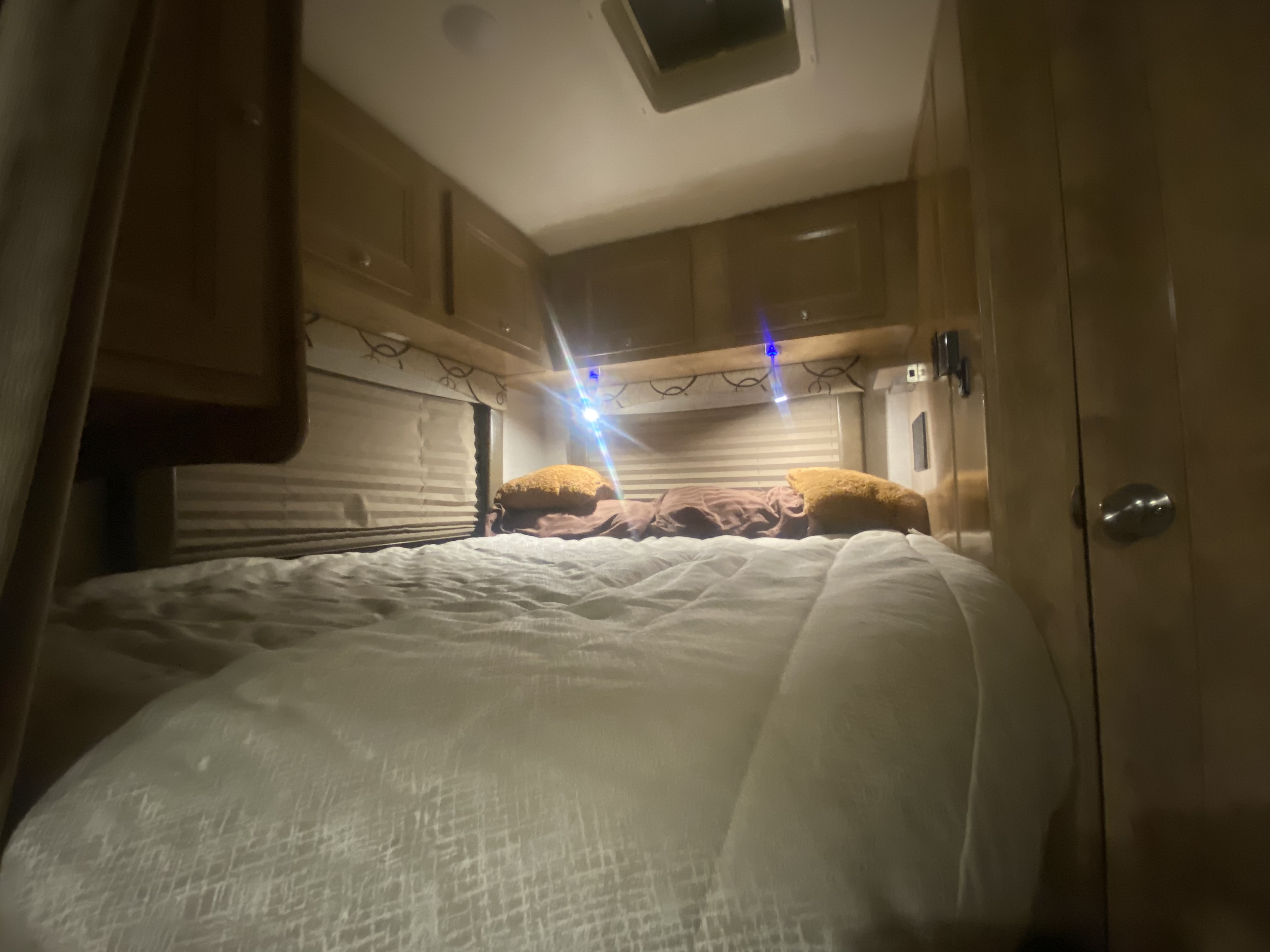 Cozy RV rental bedroom with a comfortable bed, overhead cabinets, and blinds, perfect for your journey.. Forest River Coachmen Leprechaun 2020