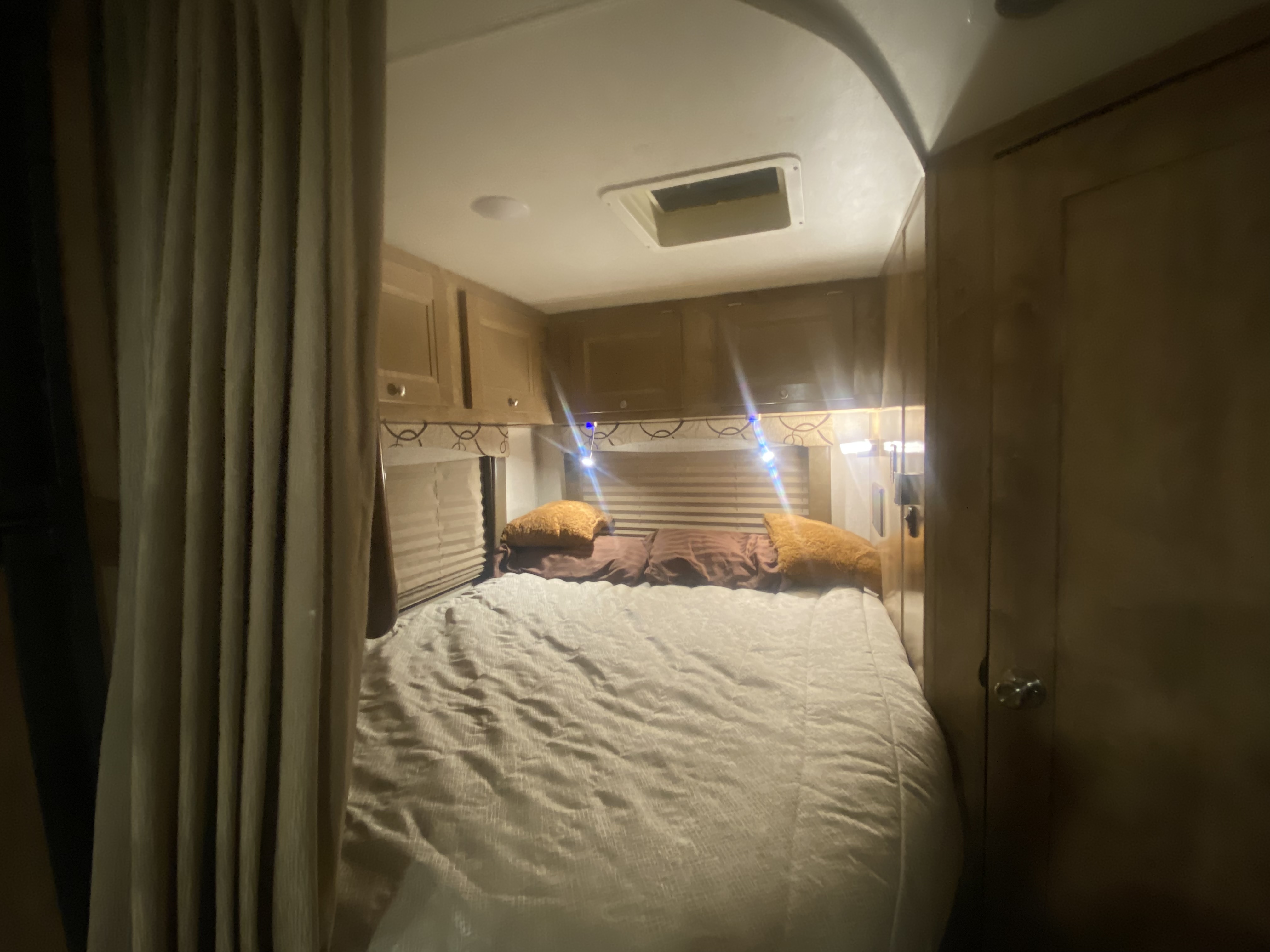 Cozy RV rental bedroom featuring a bed, overhead cabinets, and warm lights. Ideal for comfortable travel.. Forest River Coachmen Leprechaun 2020