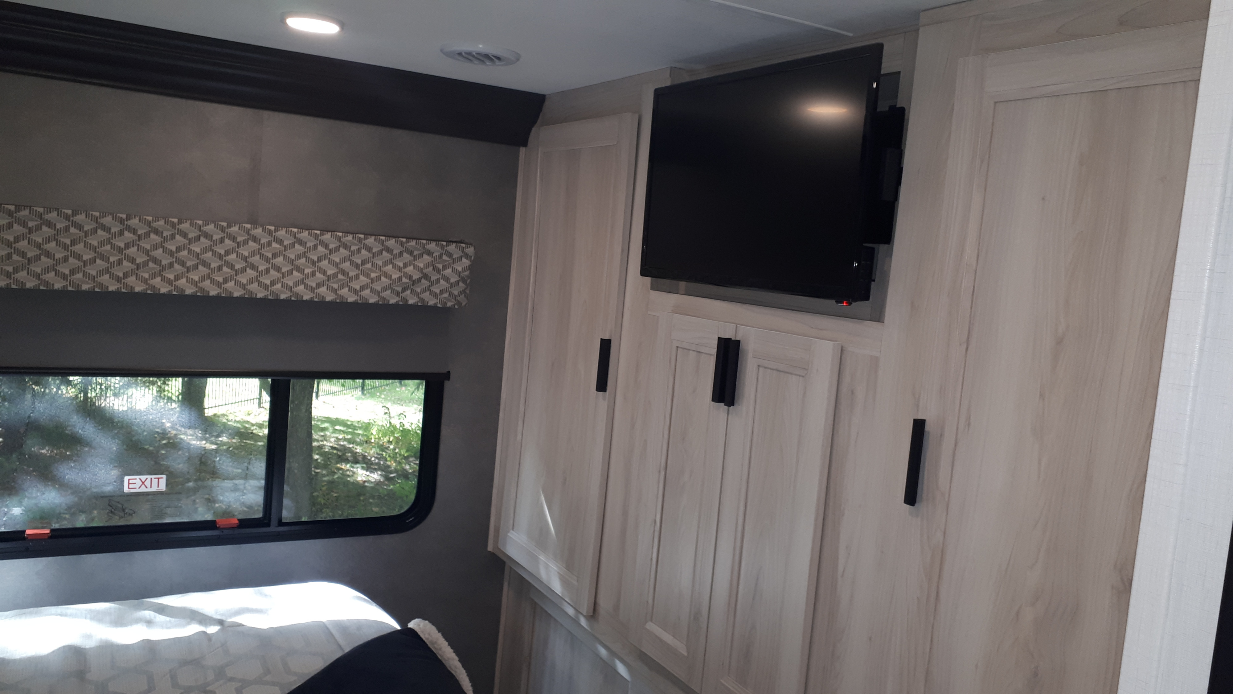 Modern RV rental interior: bedroom with wall-mounted TV, light wood cabinets, and an emergency exit window.. Forest River Classic 3011DS 2023