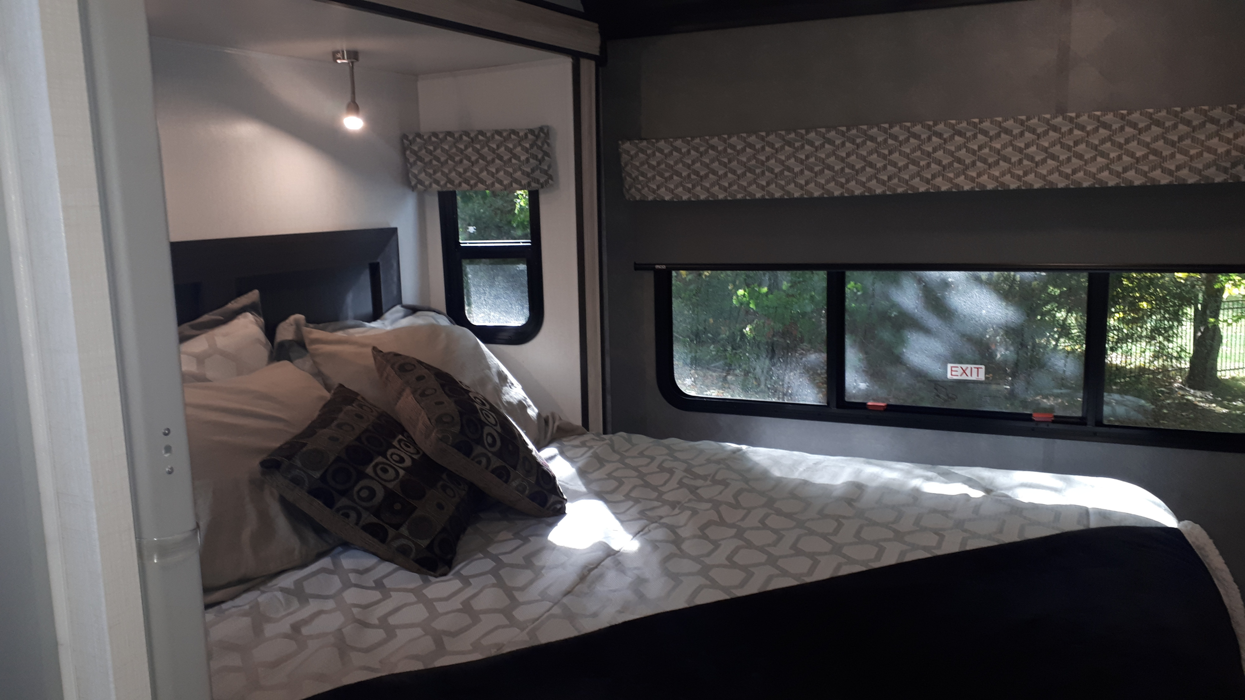 Bright RV rental bedroom: A cozy bed with patterned bedding, pillows, and sunlit windows revealing leafy green outdoor views.. Forest River Classic 3011DS 2023