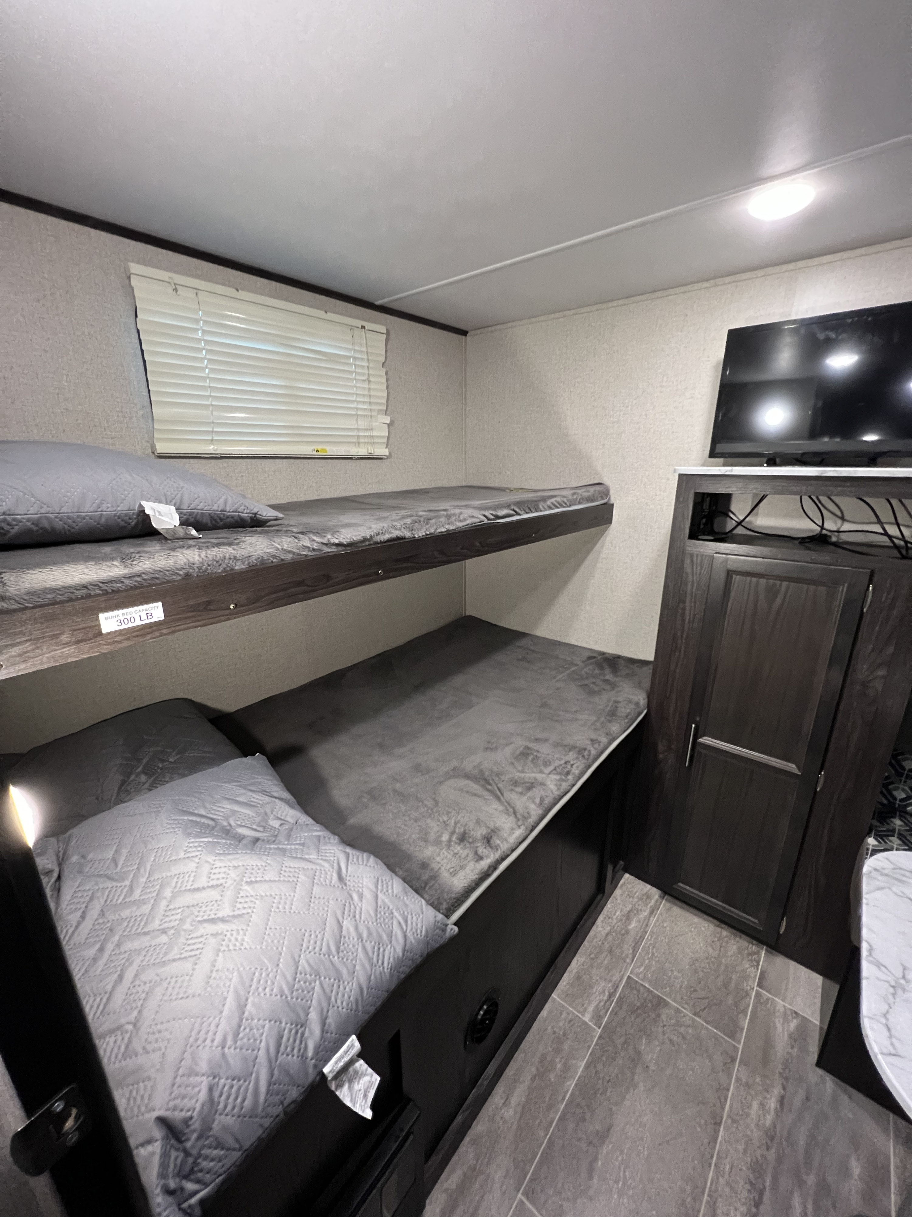 Cozy RV rental interior showcasing practical bunk beds, a window with blinds, TV, and storage. Bunk capacity: 300 lbs.. Dutchmen Kodiak Ultra Lite 2020