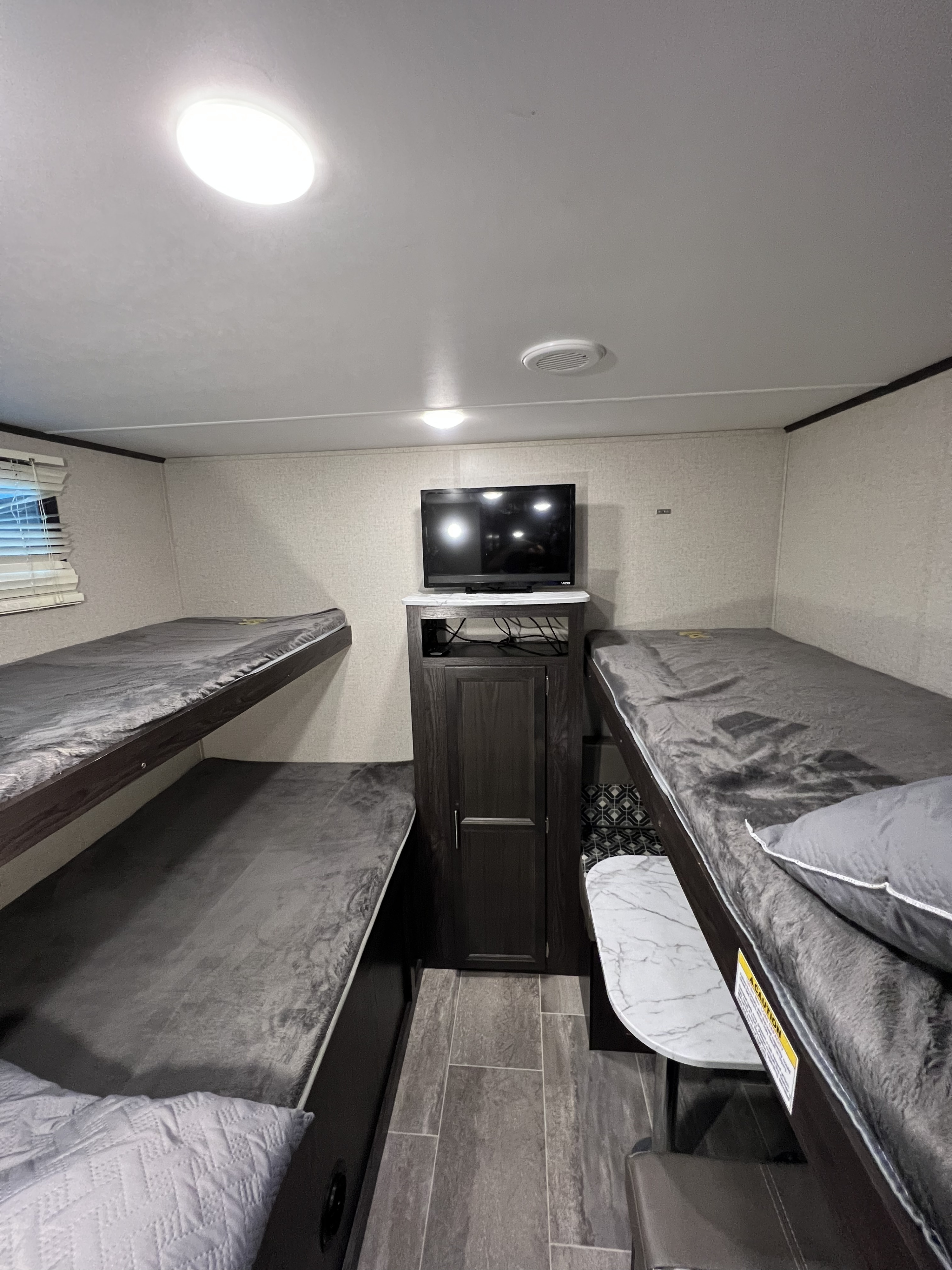 This RV rental interior features practical bunk beds on both sides, a central TV, and stylish grey finishes, optimizing space for travel.. Dutchmen Kodiak Ultra Lite 2020