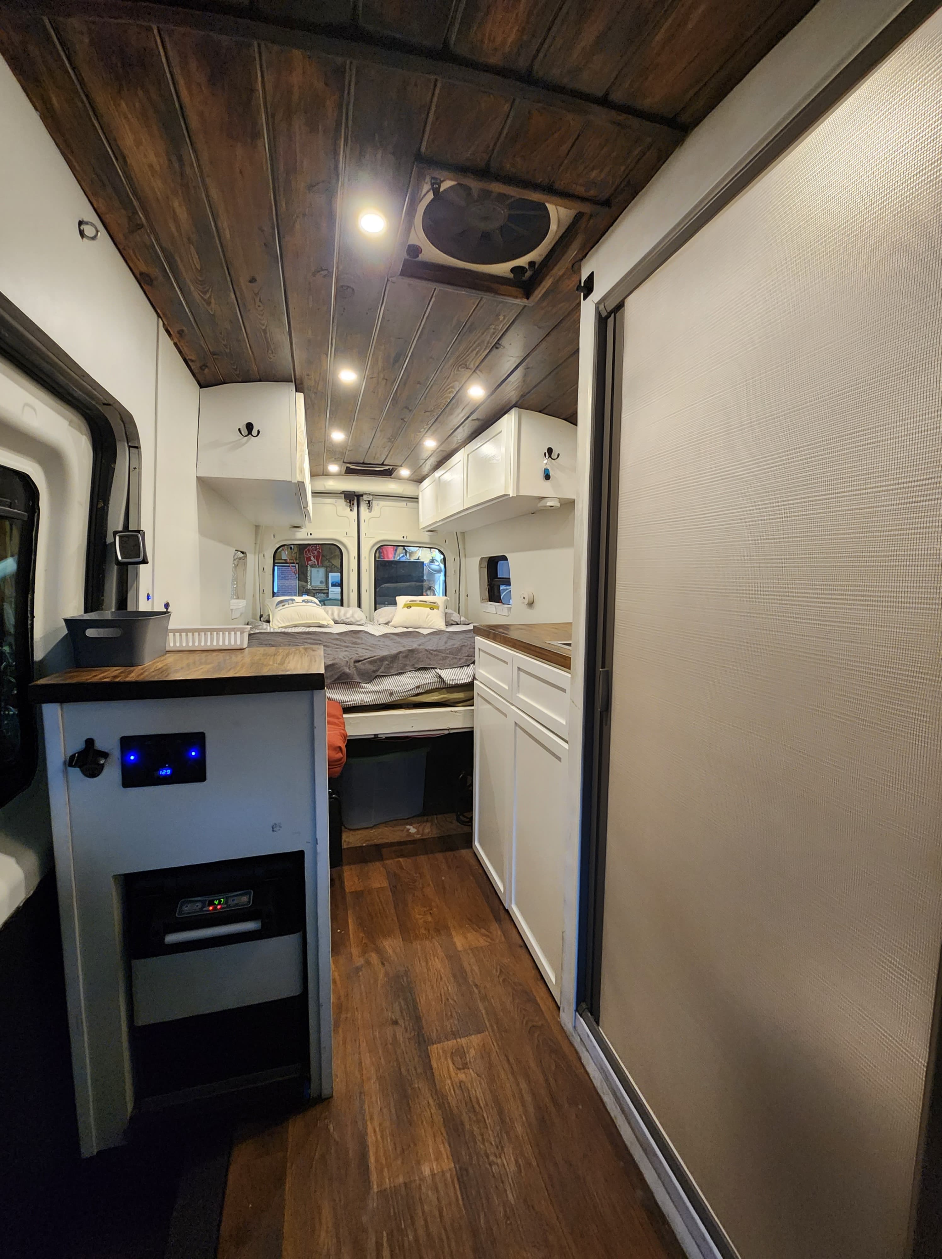 An RV rental interior showcasing a wooden ceiling, comfy bed, kitchenette, and built-in cooler for your next trip.. Ford Custom Transit 2016