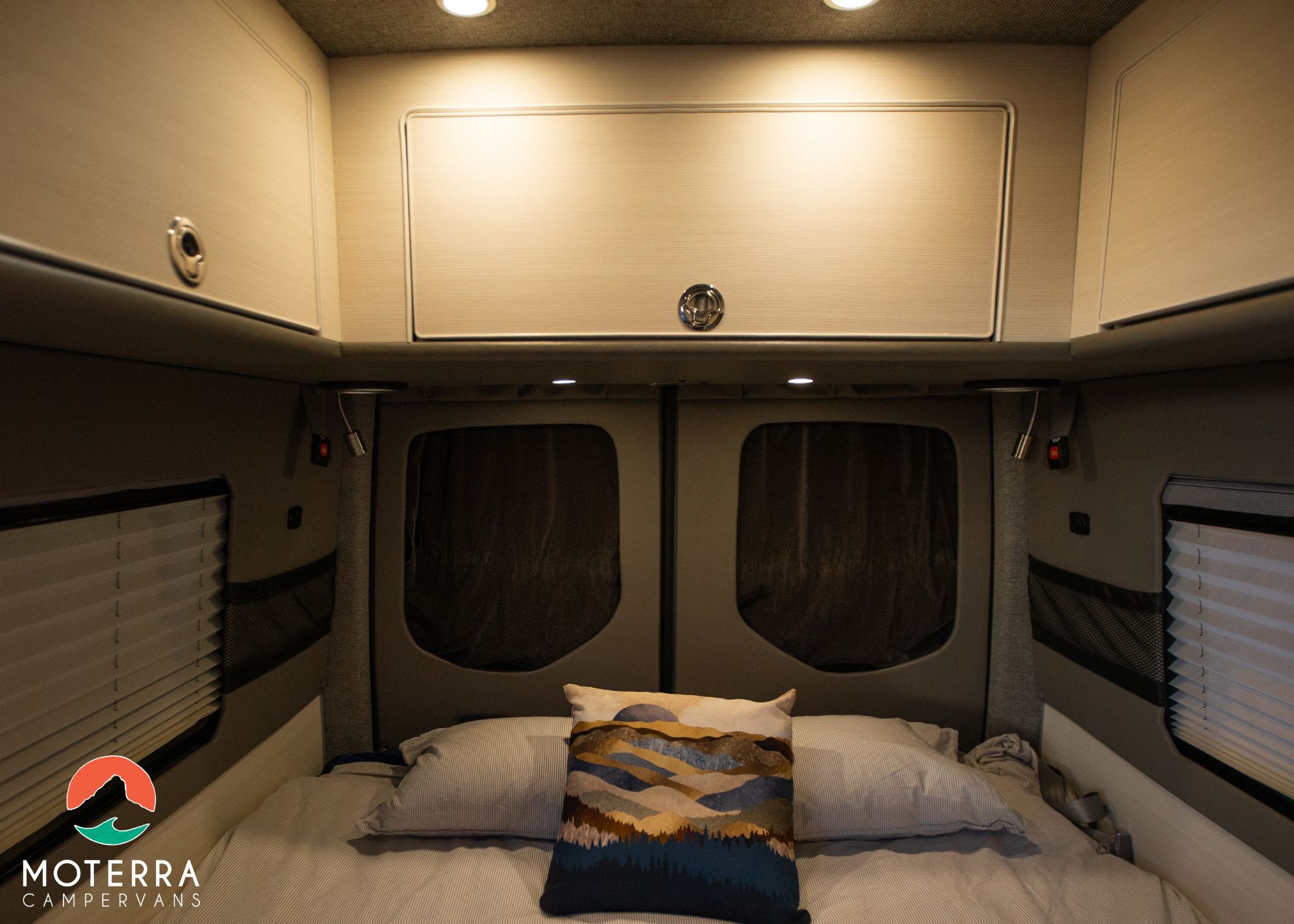 Cozy RV rental camper van interior. Features a comfortable bed with a decorative pillow, overhead storage, and warm lighting.. Mercedes-Benz Sprinter 2020