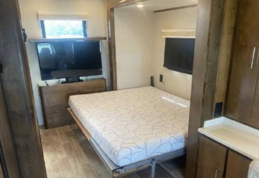 Inside an RV rental: a cozy bedroom features a TV, comfy mattress, and bright window, offering a compact travel home.. Wayfarer Wayfarer Motorhome 2019