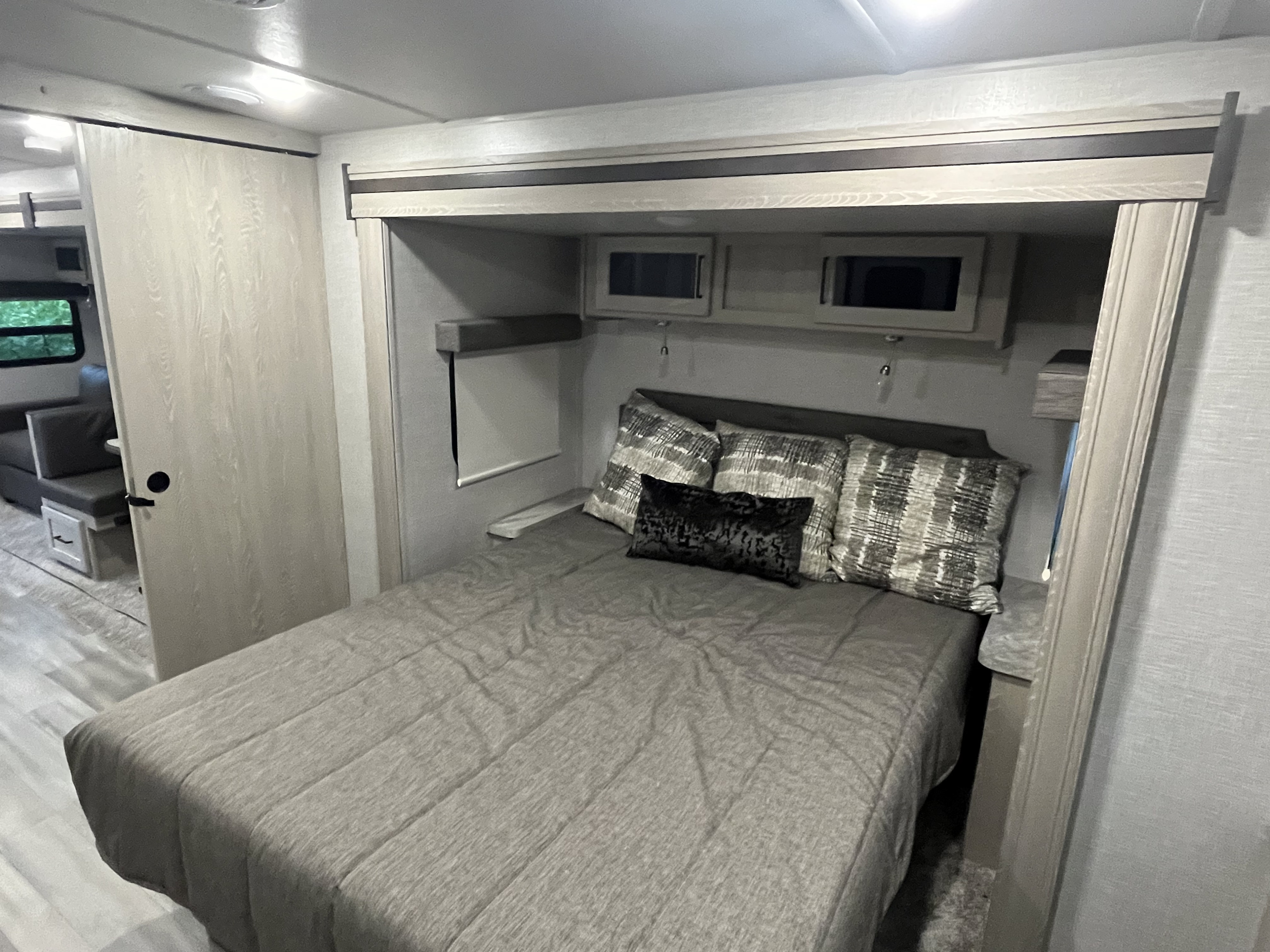 RV rental interior: Bedroom with a made bed, patterned pillows, overhead cabinets, and a sliding privacy door for comfortable sleeping.. Forest River Rockwood Ultra Lite 2021