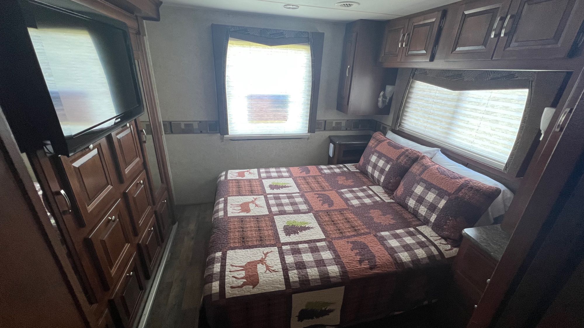 Cozy RV rental bedroom with a nature-themed quilt, TV, and rich wood cabinetry, offering comfort & storage.. Forest Rivers Georgetown 2013