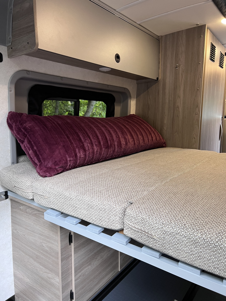 Spacious RV rental interior with a comfy bed, overhead storage, and a window for scenic views. Ideal for your next adventure.. Winnebago Solis 59PX 2023