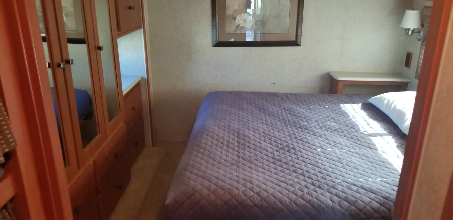 RV rental bedroom featuring a comfortable quilted bed, built-in storage, and warm sunlight.. Winnebago Sightseer 2008
