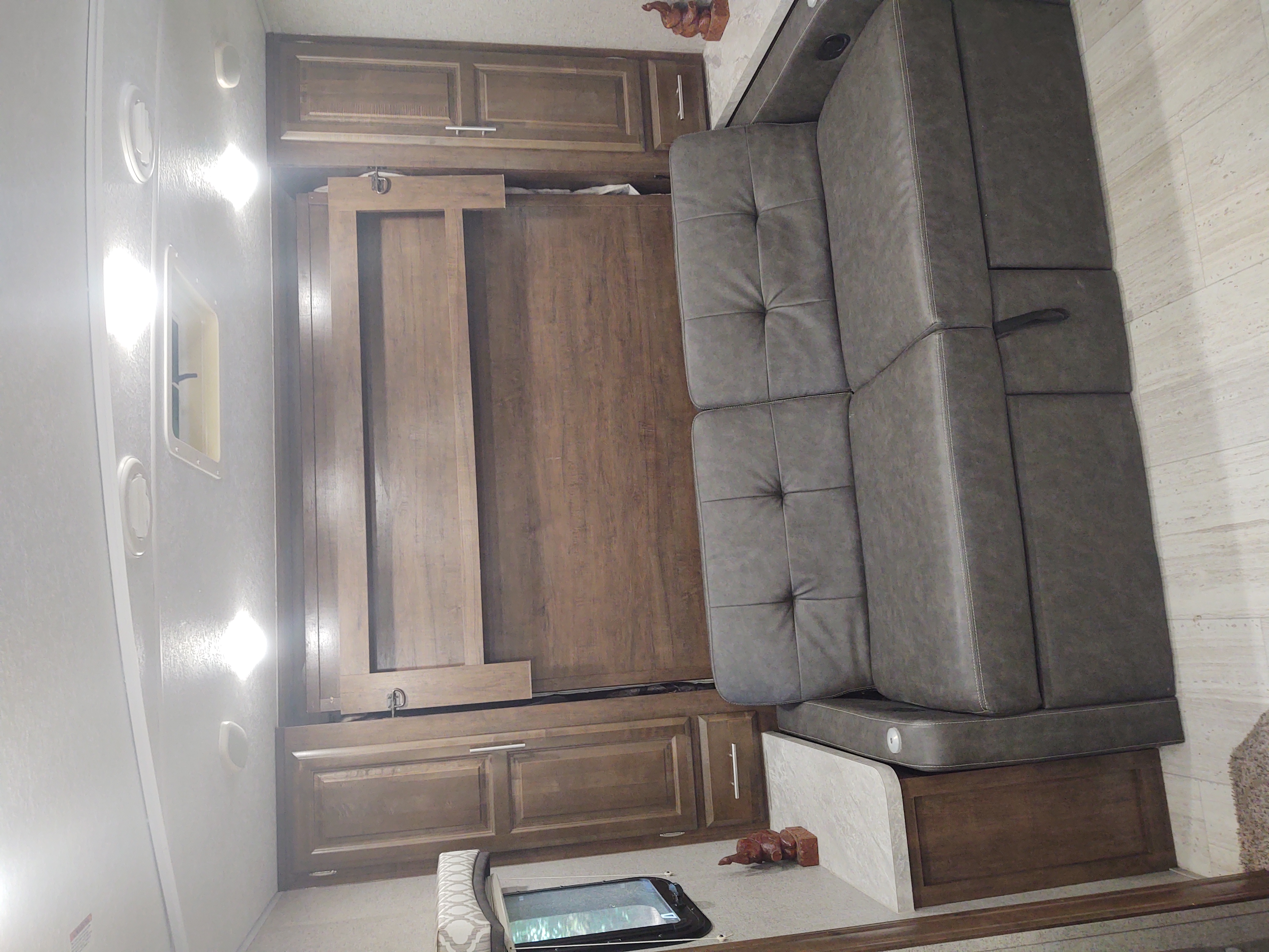 Compact RV rental interior featuring a gray tufted sofa, wooden cabinets, and a clever pull-down bed panel for versatile living space.. Forest River Flagstaff Micro Lite 2019