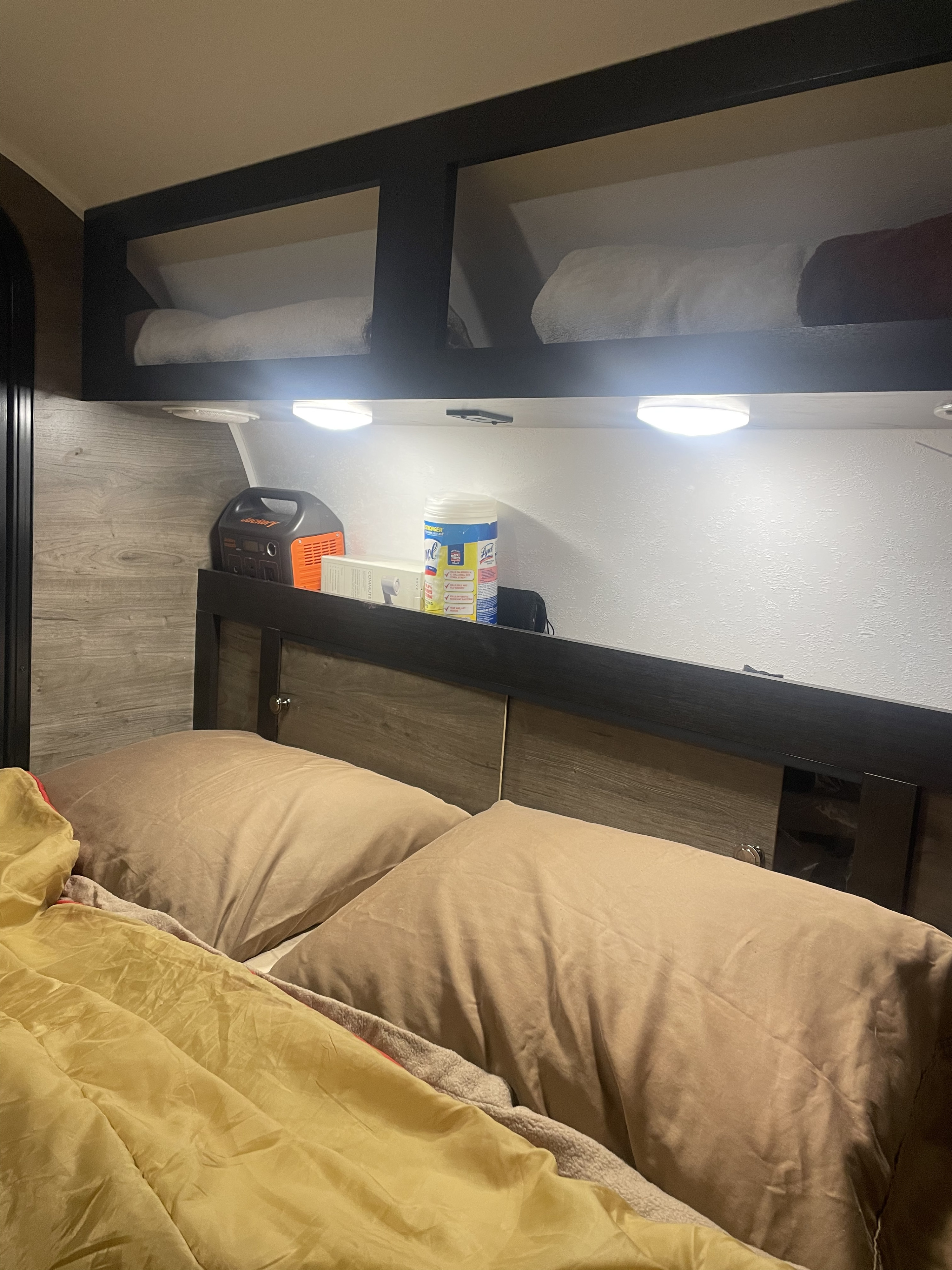 RV rental bed with pillows & yellow comforter. Illuminated overhead storage holds Jackery and Lysol wipes.. Braxton Creek Free Solo 2022