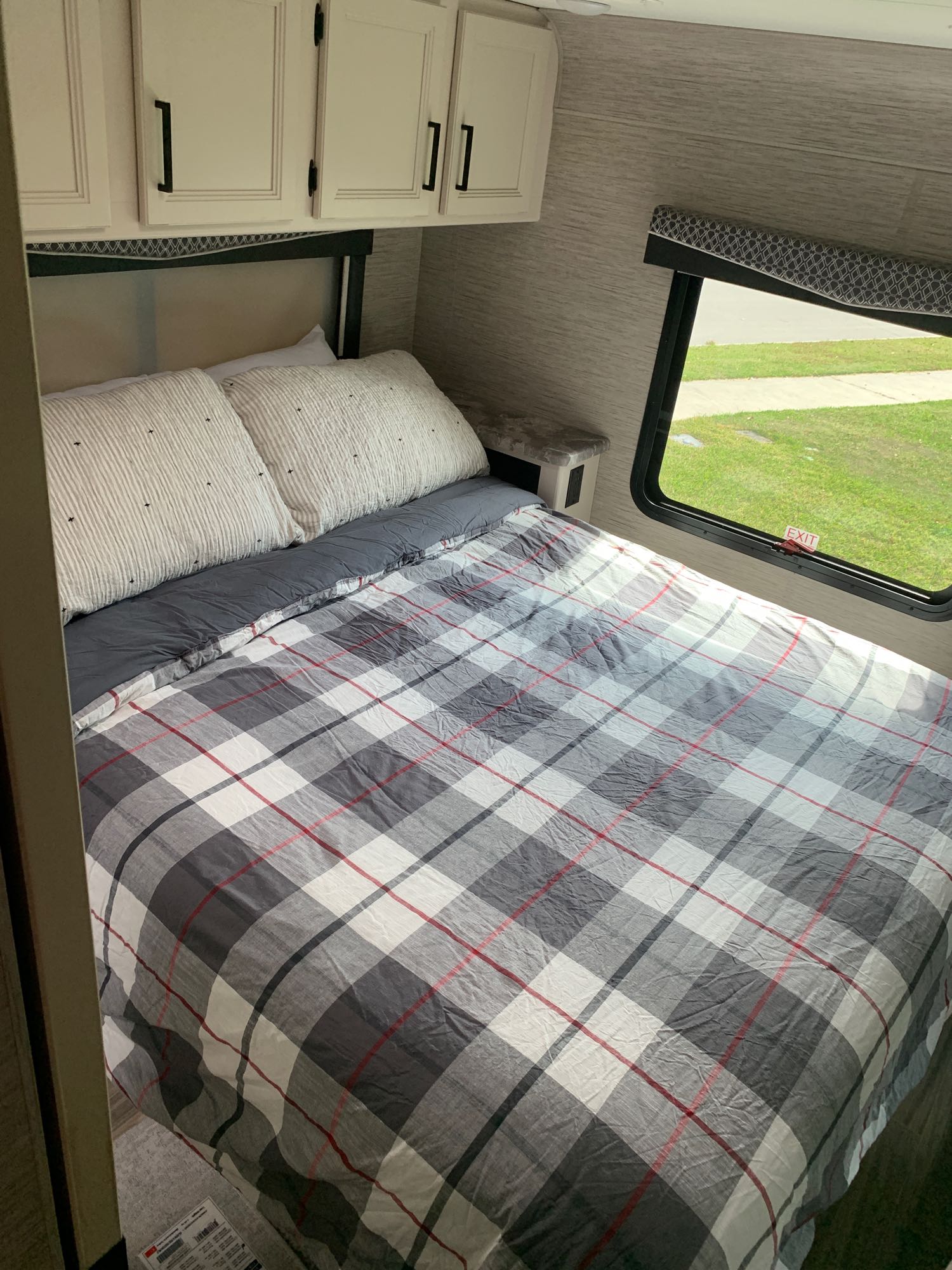 This cozy RV bedroom features a bed with plaid bedding, striped pillows, and overhead cabinets, ideal for an RV rental stay.. Thor Four Winds 2022