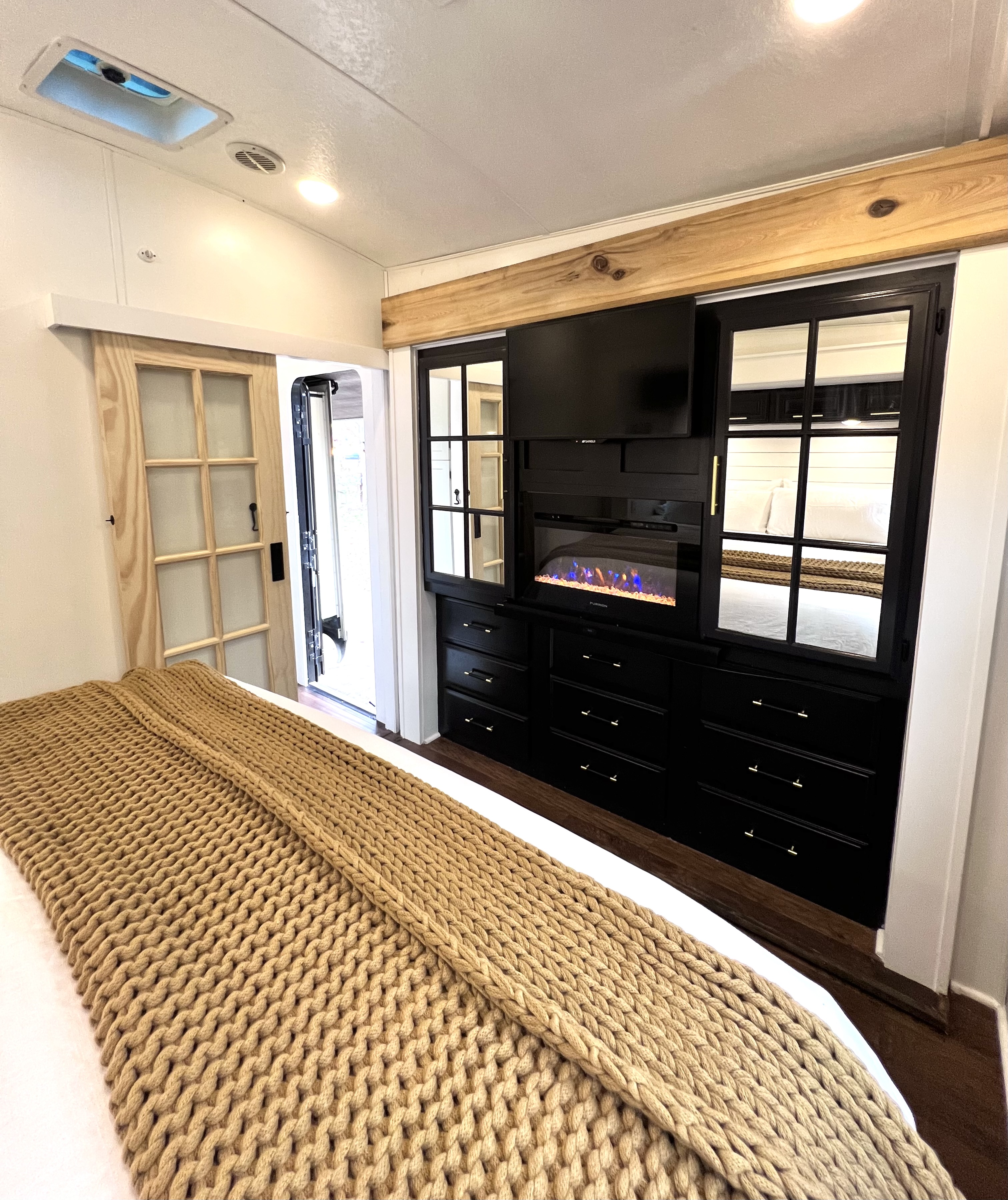 Stylish RV rental bedroom features a built-in entertainment unit with a fireplace, a comfy bed with a knit blanket, and a barn door.. Keystone RV Montana 2015