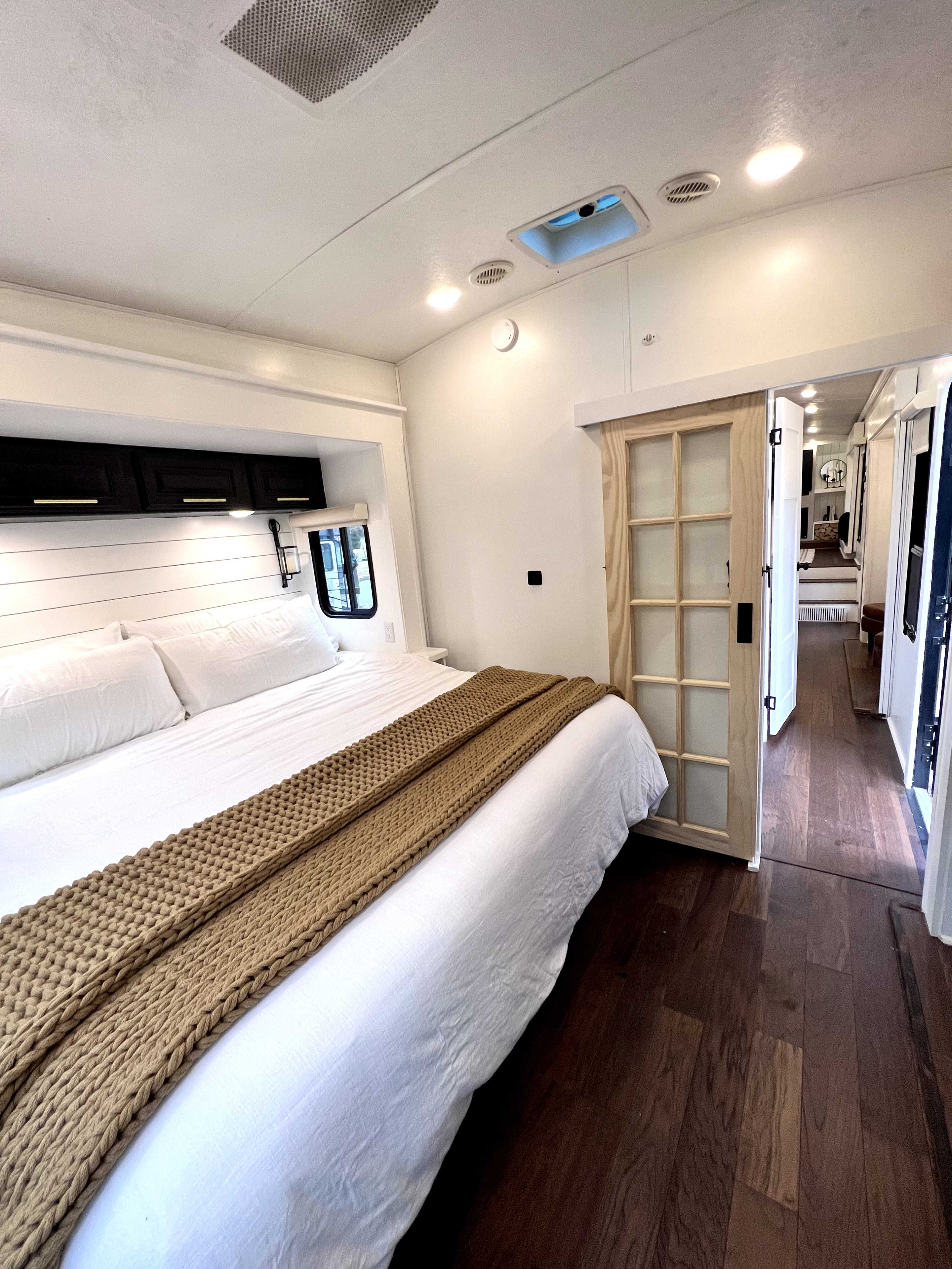Modern RV rental bedroom with white bed, cozy brown blanket, sleek black cabinets, and barn door.. Keystone RV Montana 2015