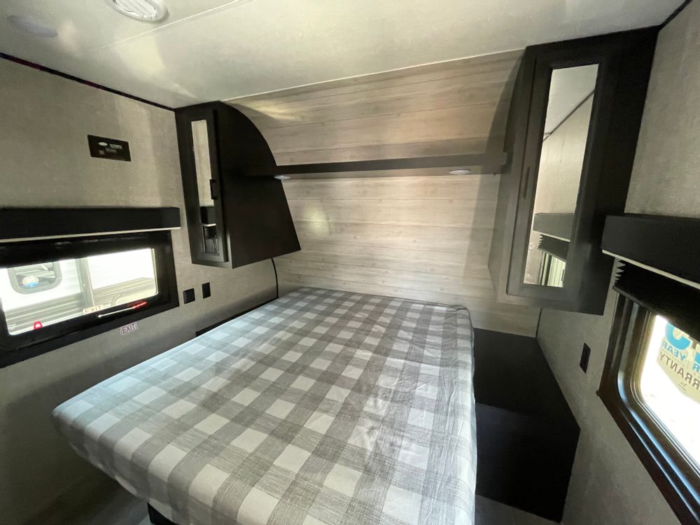Bright RV rental bedroom features a comfy checkered bed, overhead cabinets, and dual windows.. Jayco Jay Flight SLX 2022