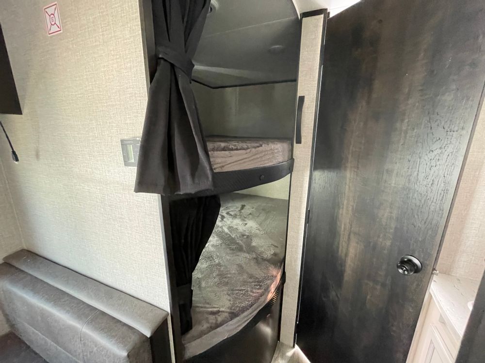 Cozy RV rental interior featuring comfortable bunk beds with privacy curtains and a built-in seating area.. Jayco Jay Flight SLX 2022