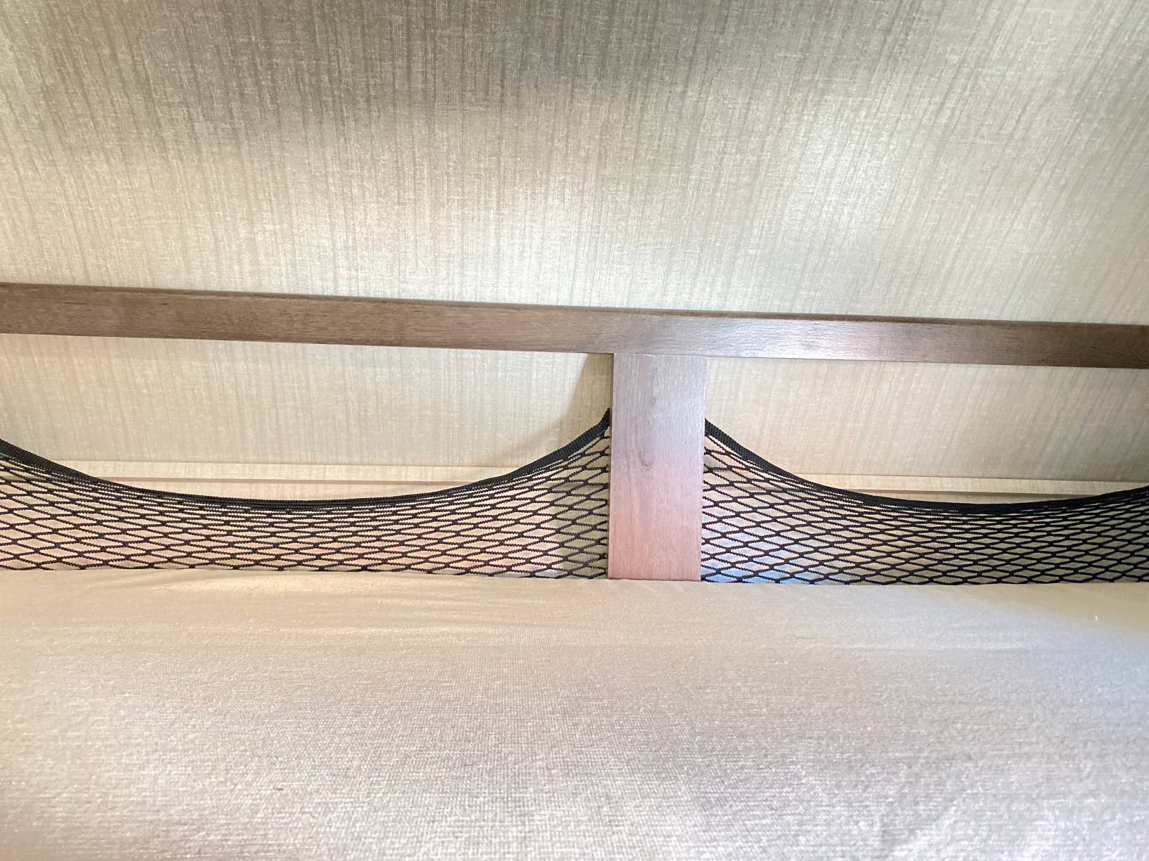RV rental interior: Light-toned bunk with wooden frame & black mesh storage net positioned over a bed.. Jayco Redhawk 2018