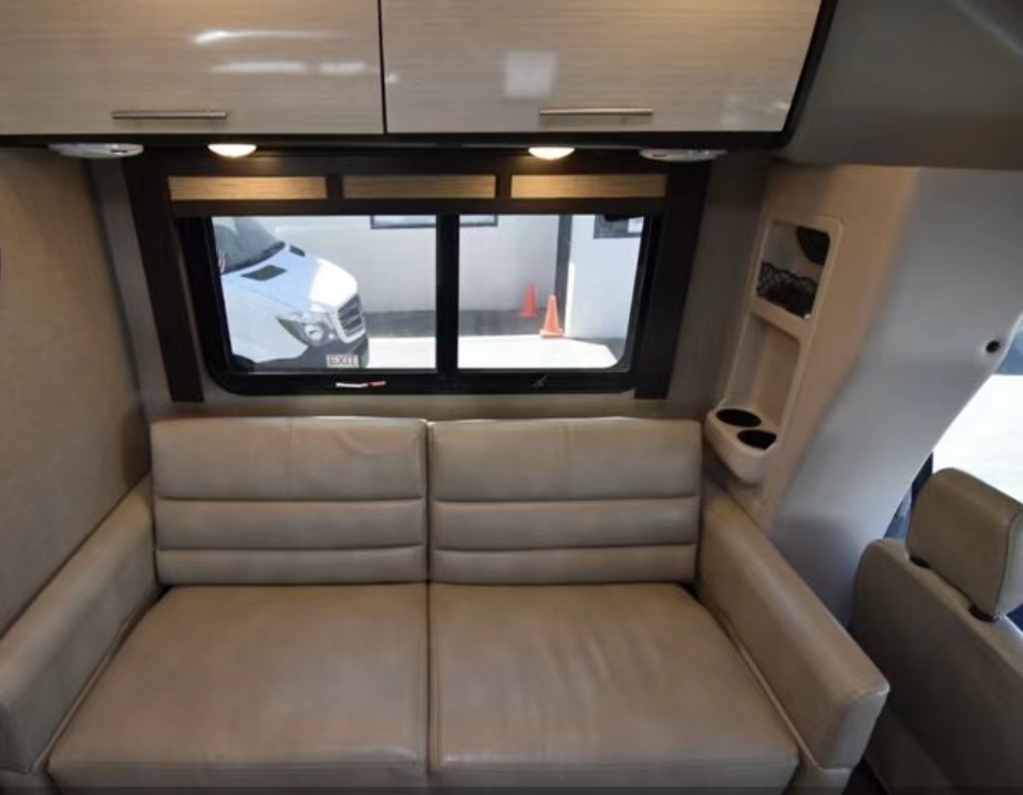 RV rental's inviting interior: comfortable beige sofa, overhead cabinets, and a side panel with cupholders and a window.. Thor Compass 2018