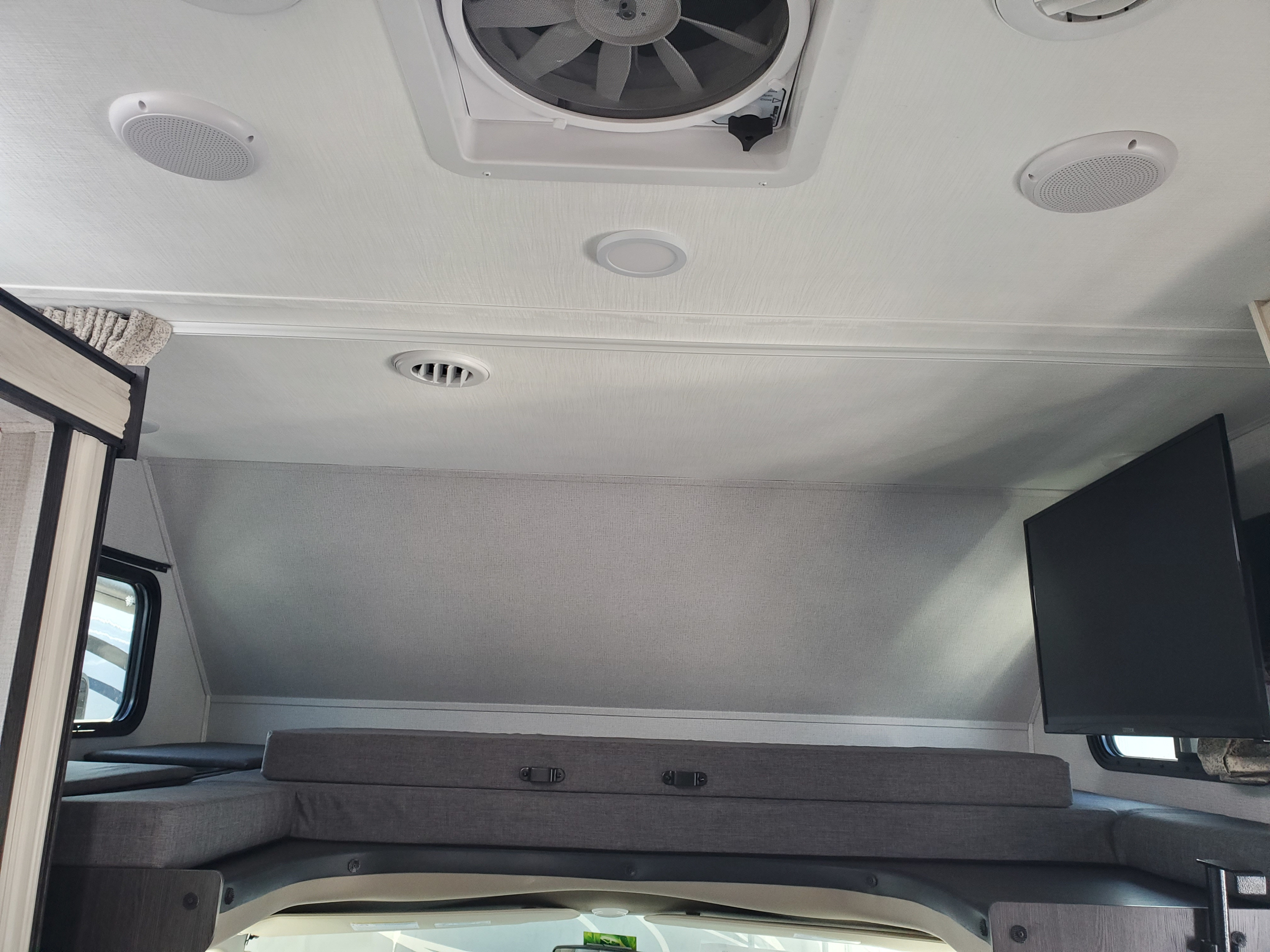 Cozy RV rental interior: view of overhead bunk with gray cushions, wall-mounted TV, ceiling fan, air vent, and speakers.. Forest River Sunseeker 2020
