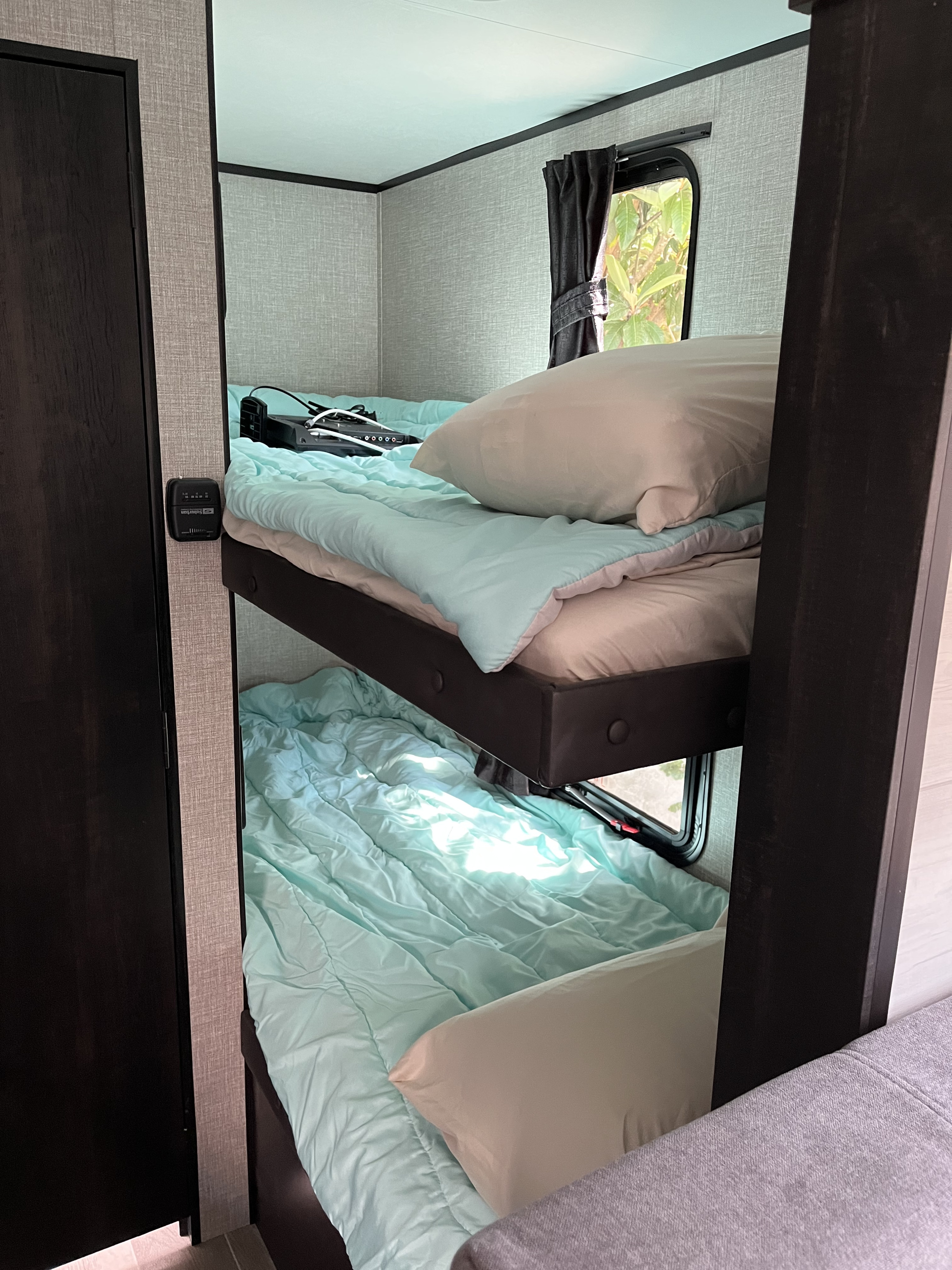 RV rental interior: cozy bunk beds with light blue comforters, a laptop on the top bunk, and a thermostat on the wall.. Jayco 184bs Bunk House Jay Flight SLX 2022