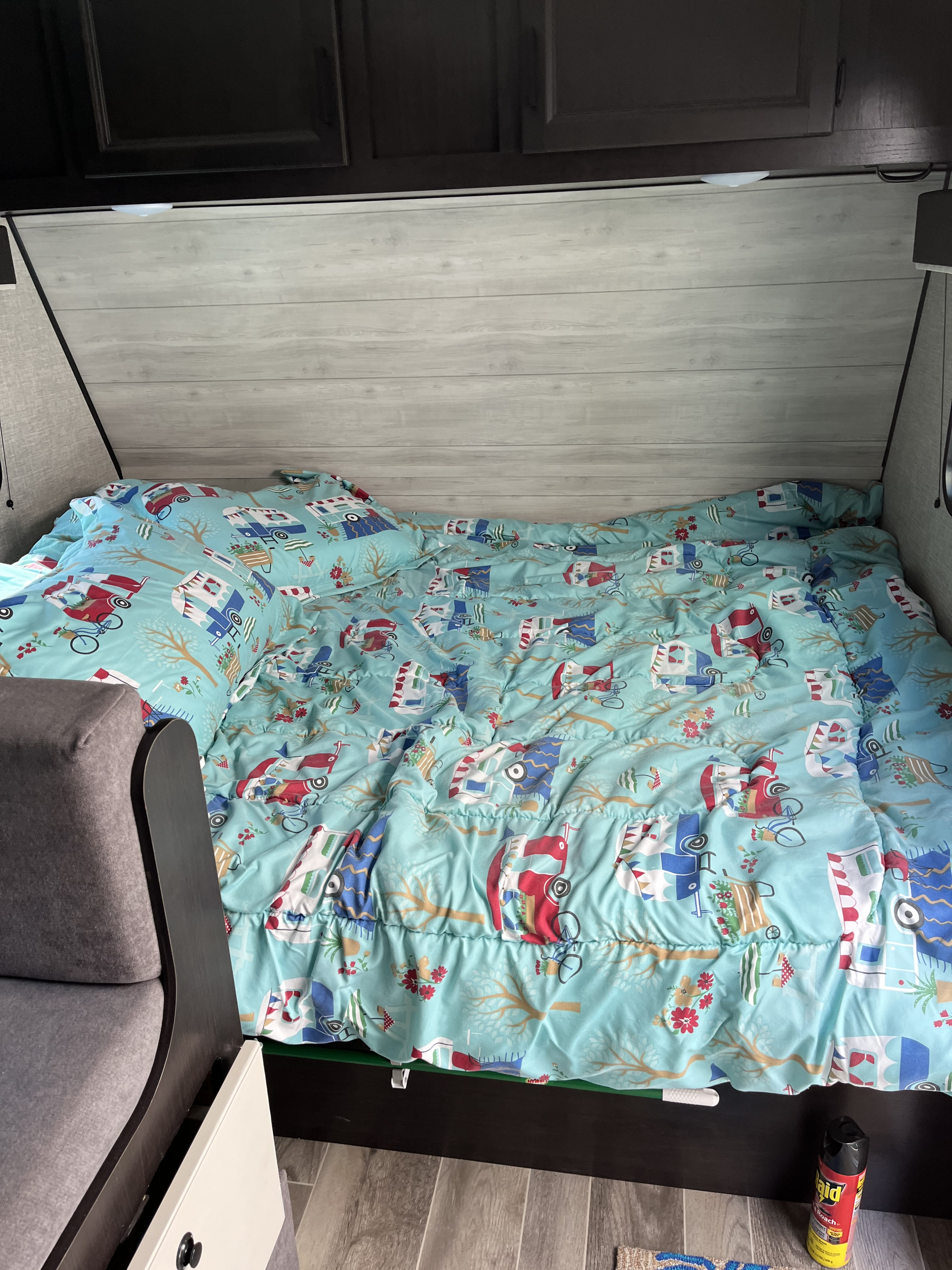 Inside an RV rental: a comfortable bed with cheerful camper-themed bedding. Overhead cabinets and a side seat are visible.. Jayco 184bs Bunk House Jay Flight SLX 2022
