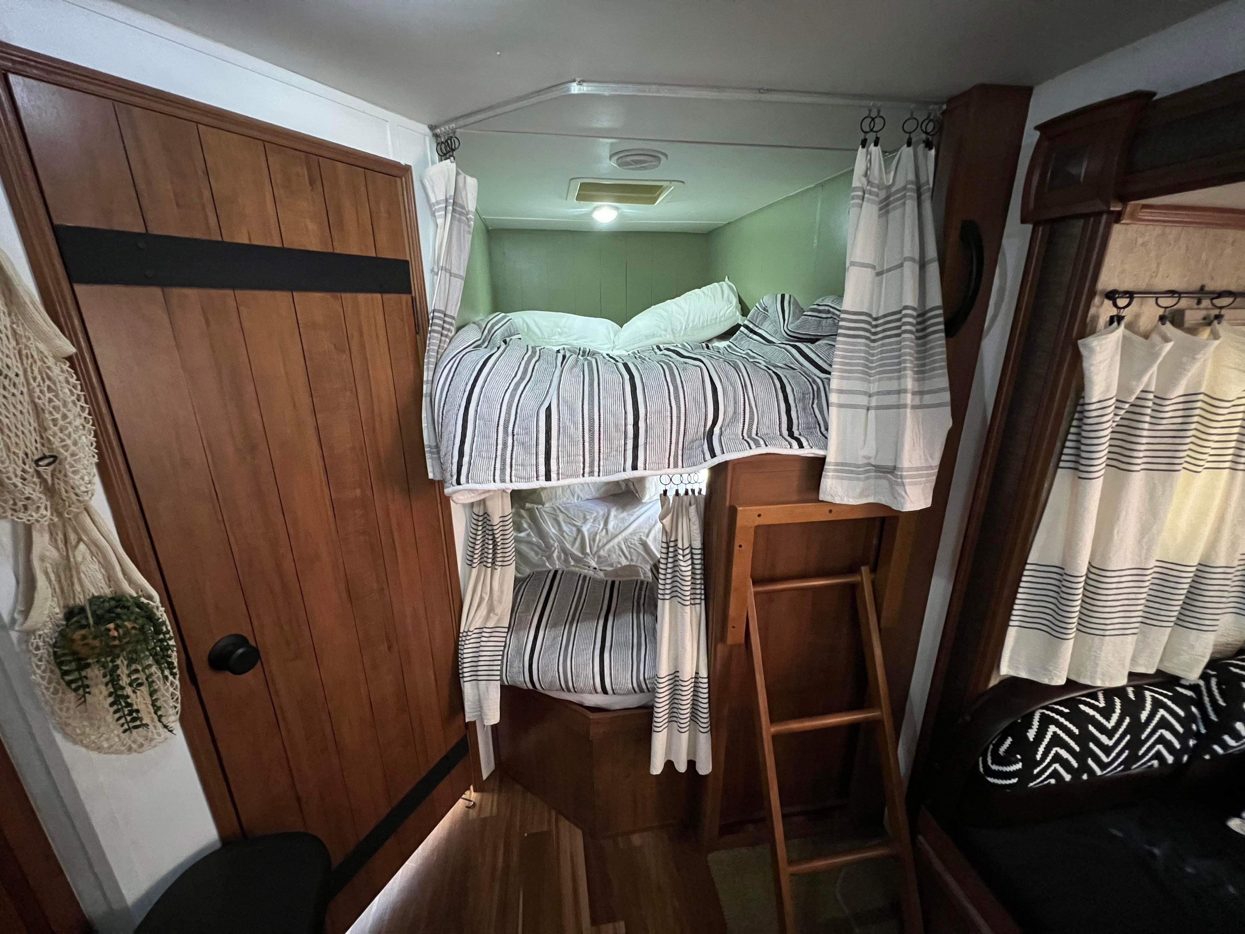 RV rental: Cozy bunk beds with striped linens & privacy curtains, accessible by a wooden ladder, within the compact interior.. Gulf Stream Conquest 2015