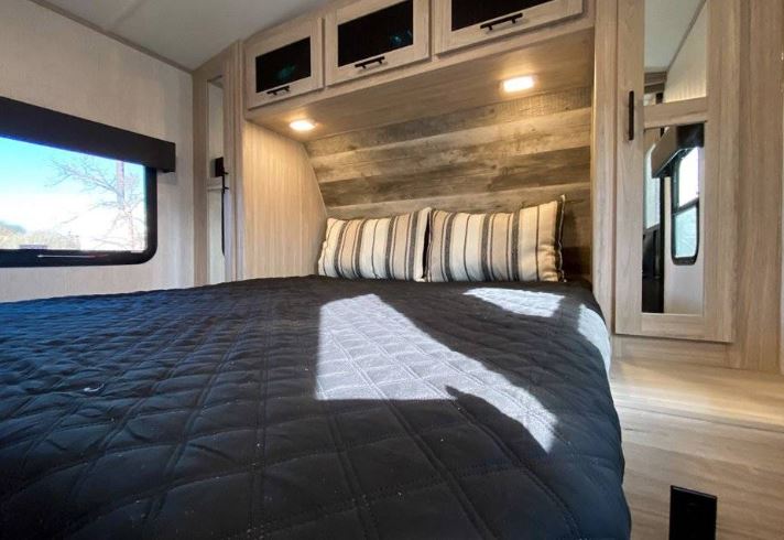 Comfortable RV rental bedroom featuring a large bed, overhead storage, mirrored wardrobe, and a scenic window view.. Heartland Sundance 2022