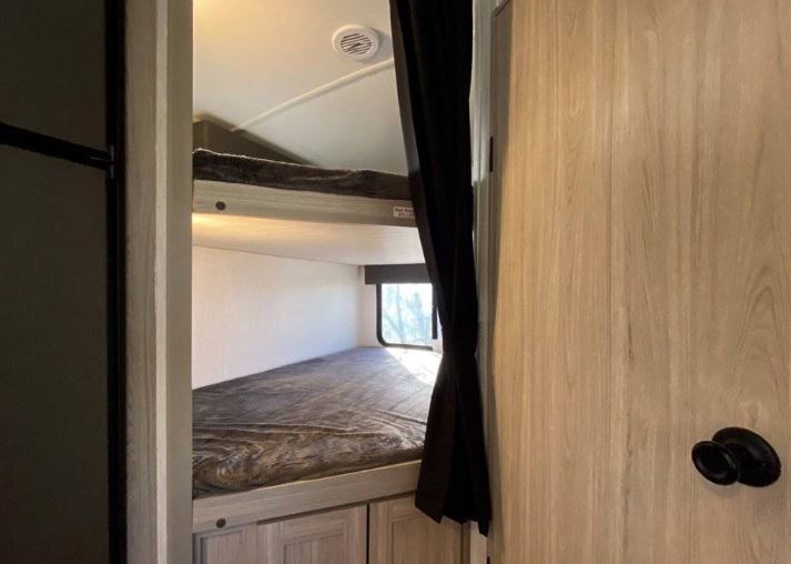 This RV rental offers a practical bunk bed sleeping area with two mattresses, a window, and wood-look cabinetry.. Heartland Sundance 2022