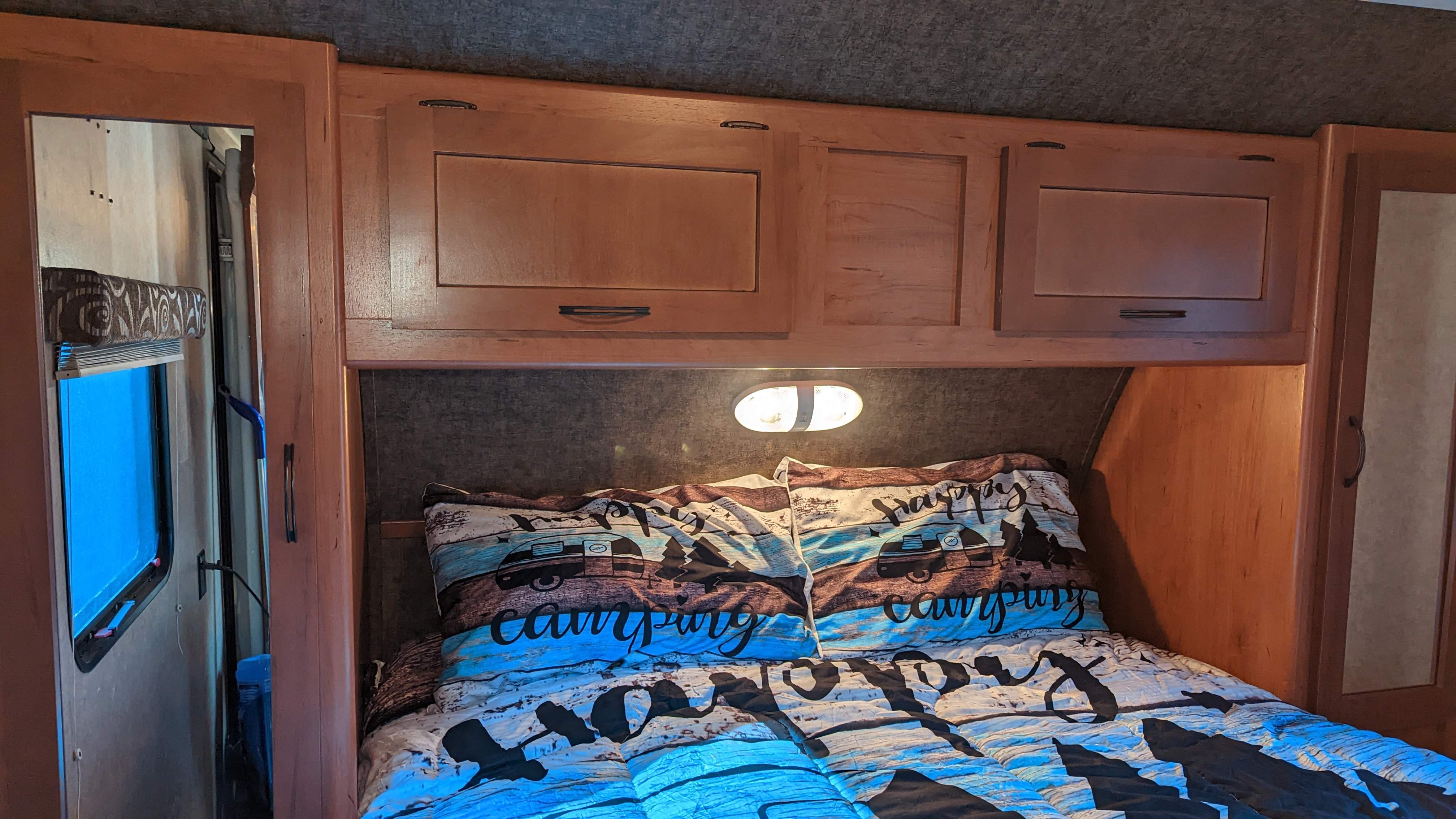 This cozy RV rental bedroom features "Happy Camping" bedding, overhead wooden cabinets, and a window for natural light.. Forest River Cherokee Grey Wolf 2015