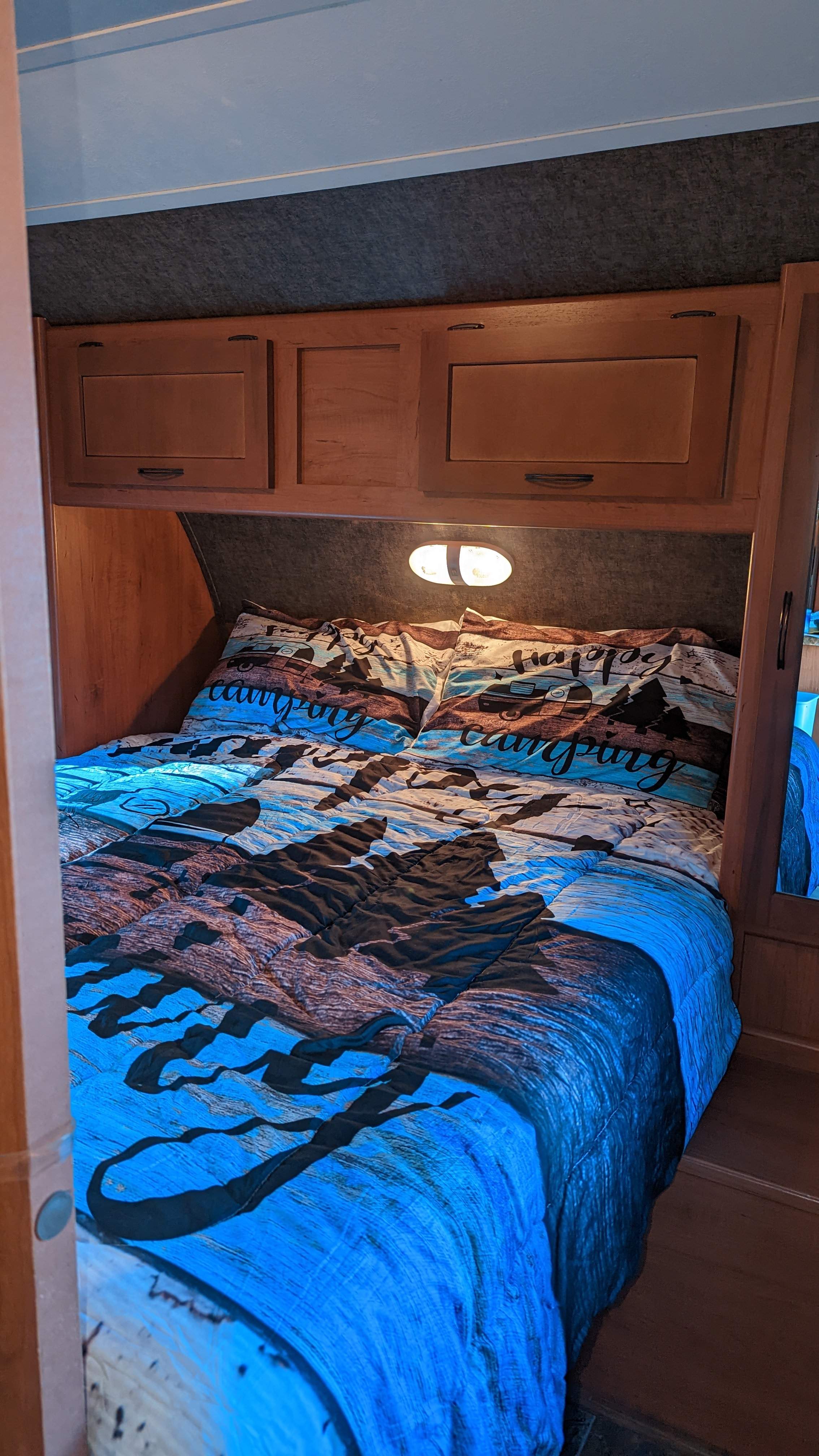 Cozy RV rental bedroom featuring "Happy Camping" bedding, overhead cabinets, and a reading light. Perfect for travel.. Forest River Cherokee Grey Wolf 2015