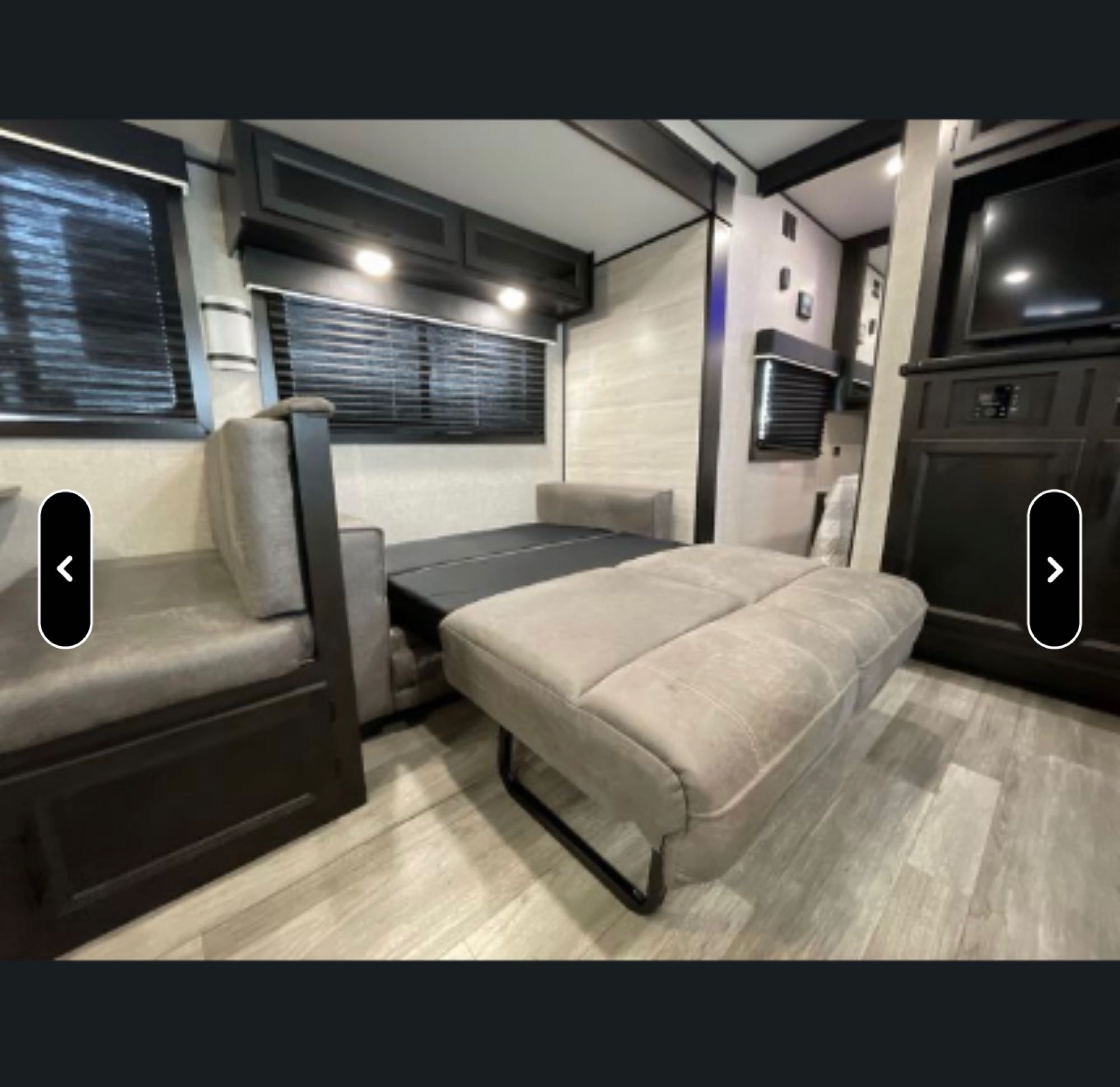 Inside an RV rental: a light-colored, pull-out sofa converts to a bed, with storage cabinets, windows, and a TV setup.. Jayco Jay Flight SLX Rocky Mountain Edition 2022