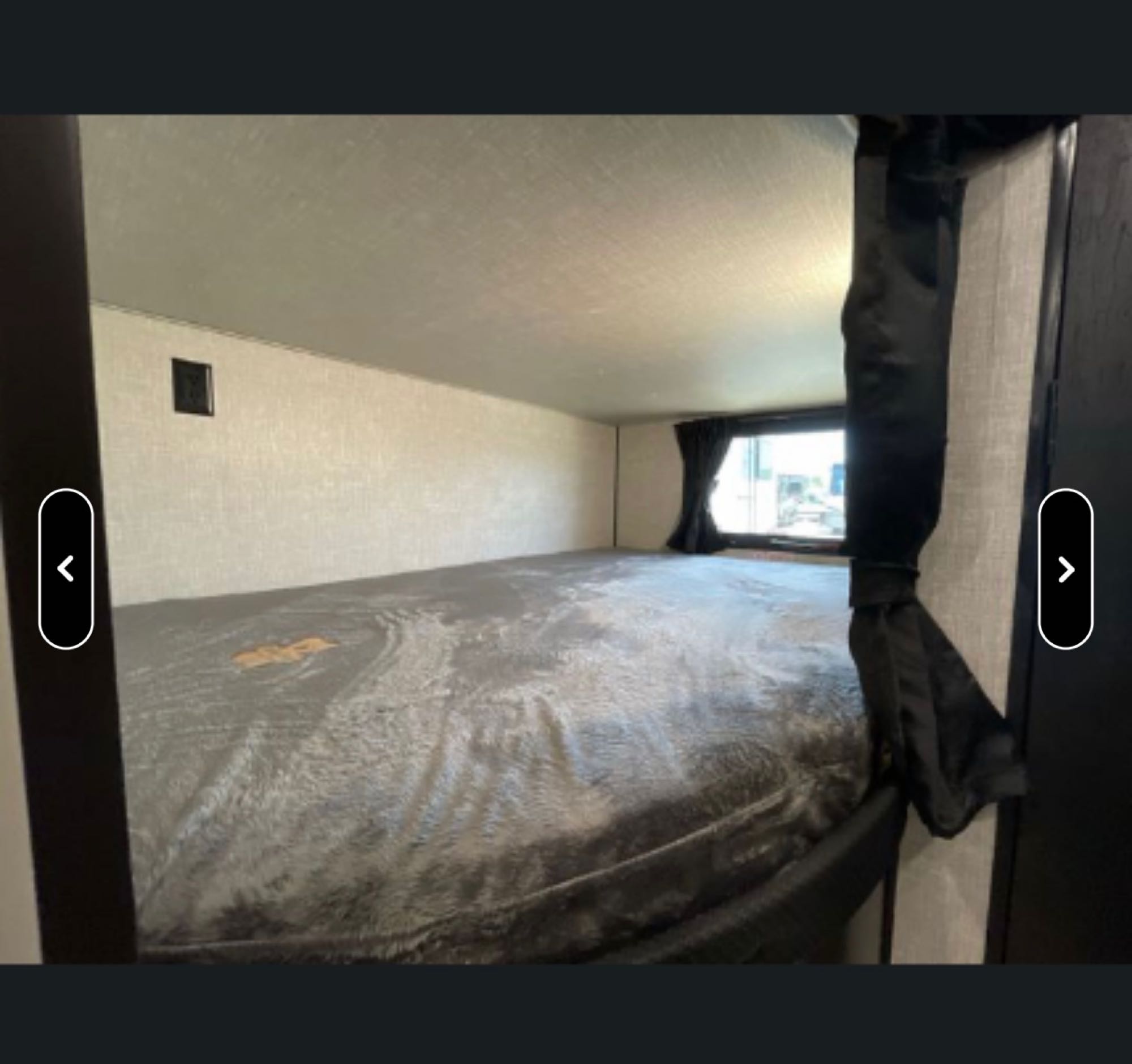 Explore this RV rental's cozy sleeping bunk, featuring a large bed with grey bedding, a window, and an outlet.. Jayco Jay Flight SLX Rocky Mountain Edition 2022