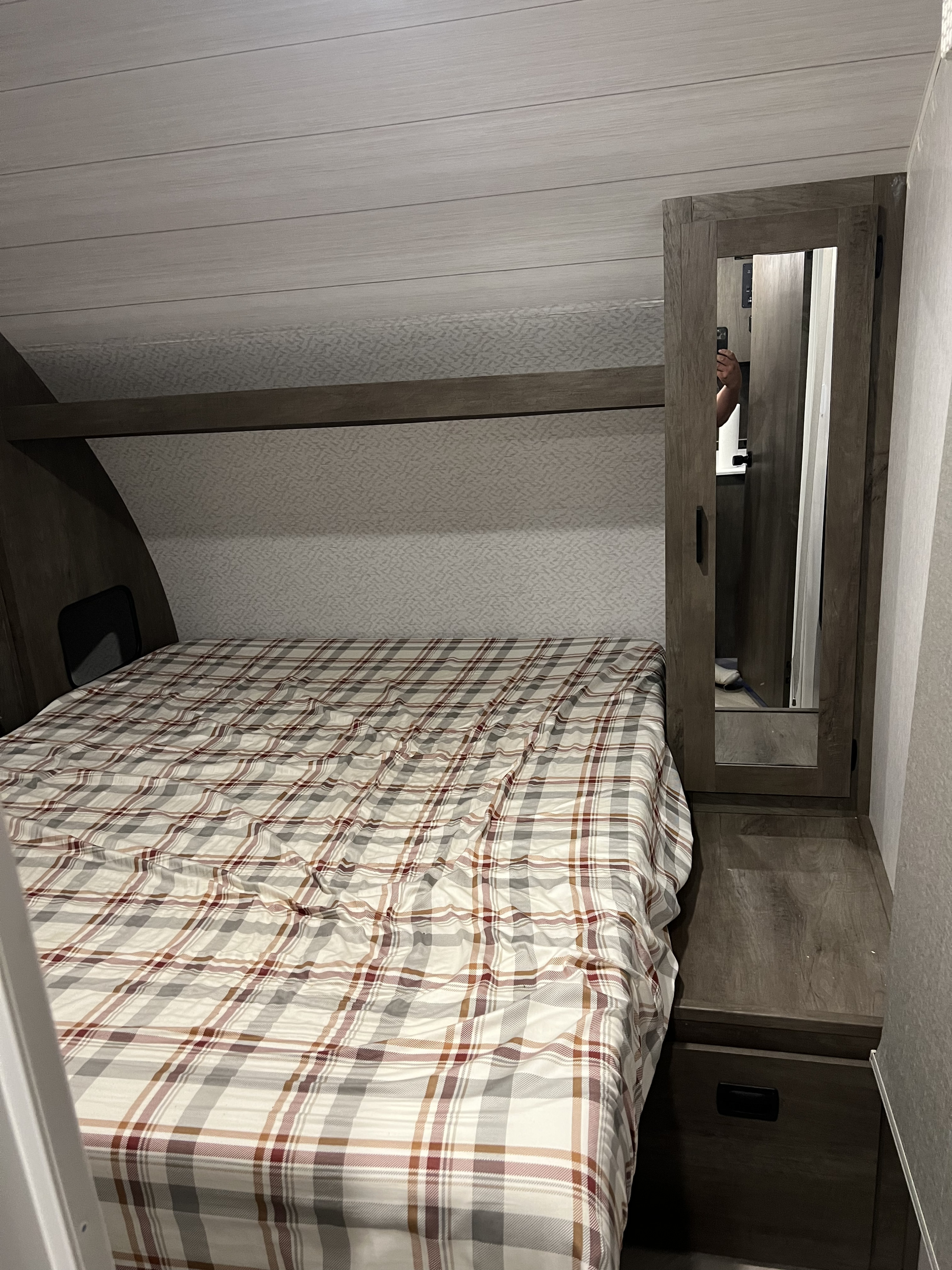 Cozy RV rental bedroom showing a plaid bed, built-in storage, wood accents, and a mirrored wardrobe door.. Forest River Wildwood X-Lite 2022