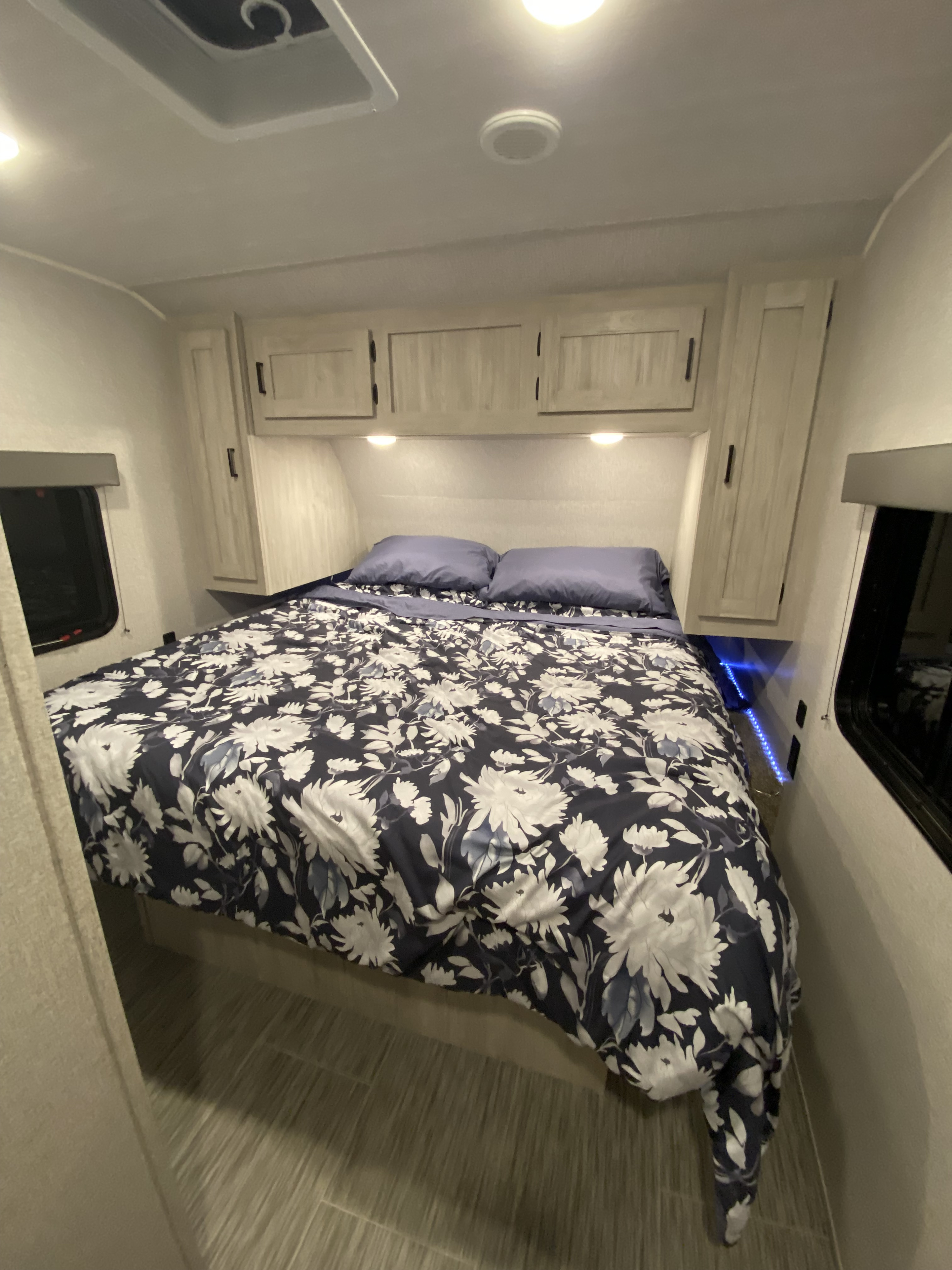 Cozy RV rental bedroom featuring floral bedding, overhead cabinets, and blue accent lighting.. East to West Silver Lake 2022