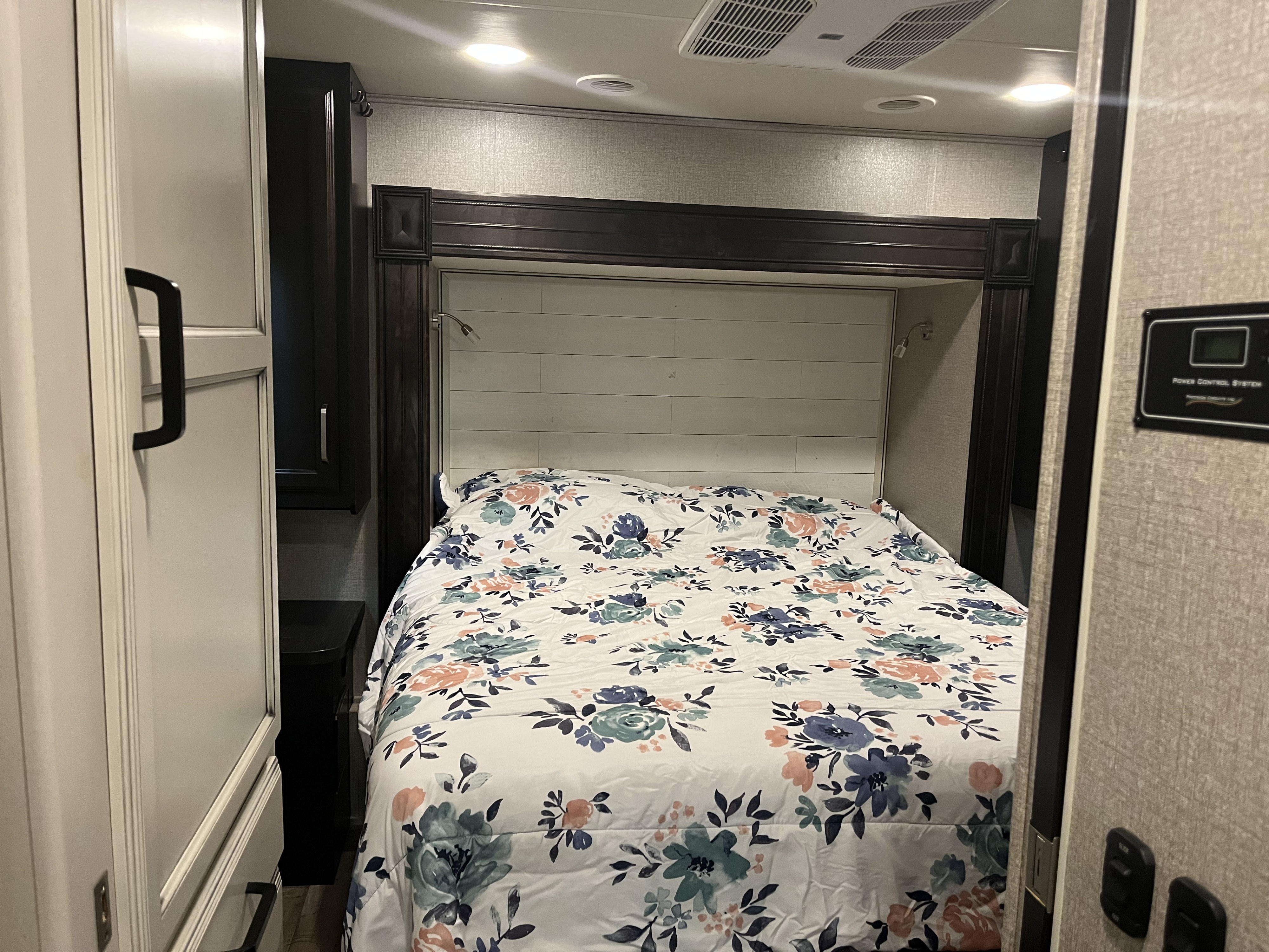 Inviting RV rental bedroom: a bed with a floral comforter, light wood headboard, dark cabinets, and ceiling lights.. Jayco Greyhawk 2021