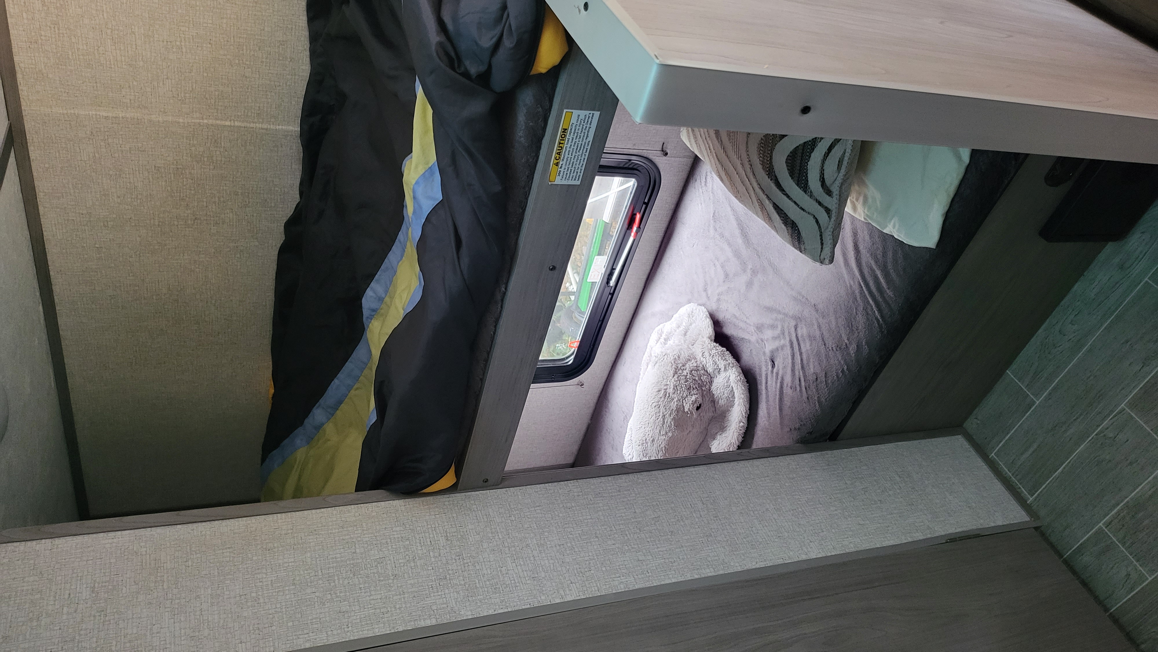 Cozy bunk beds inside an RV rental. The upper bunk has a sleeping bag; the lower bunk features gray bedding.. Keystone RV Coleman 17b 2021