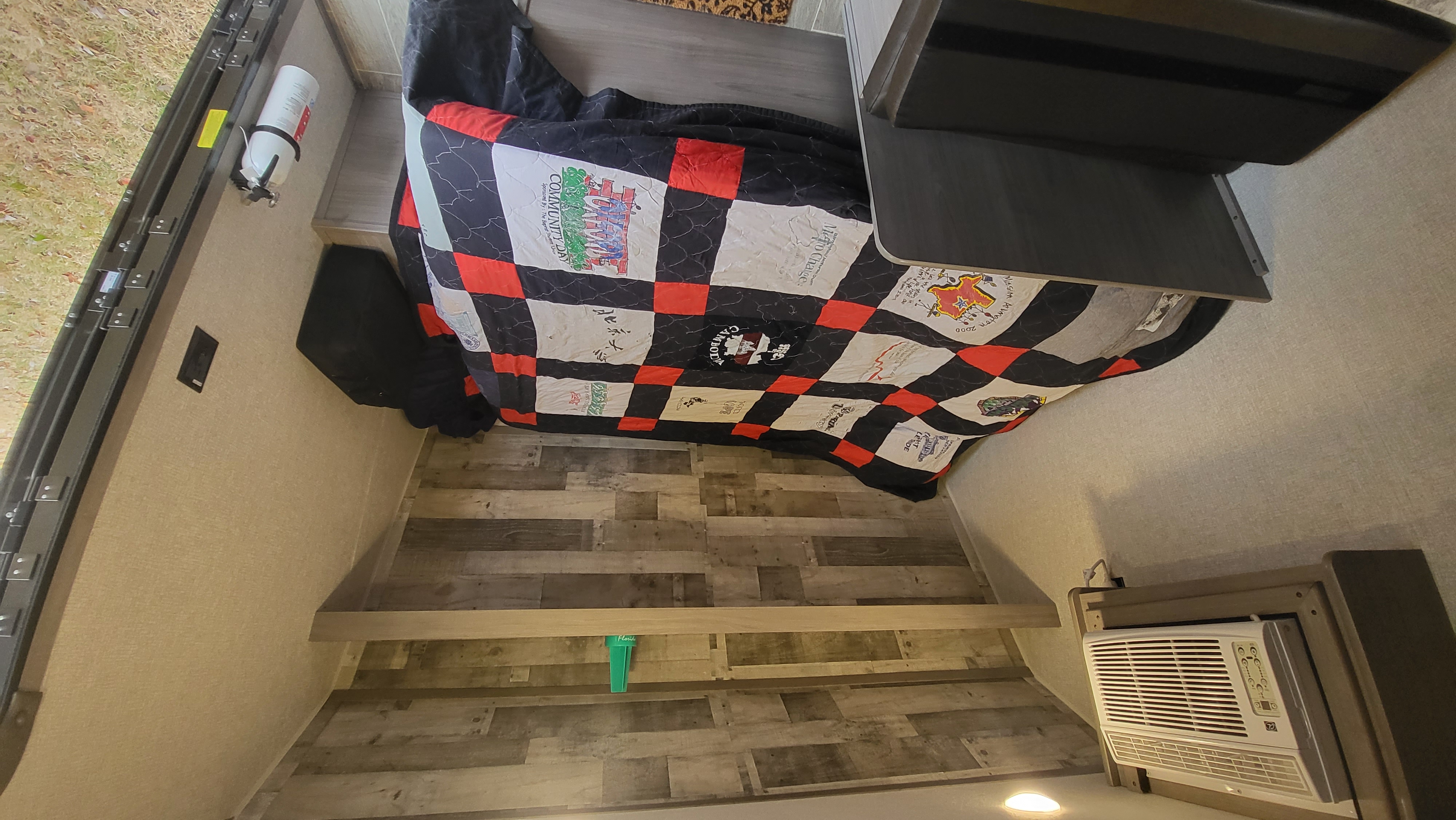 Cozy RV rental interior showcasing a bed with a unique quilt, essential fire extinguisher, and integrated AC unit.. Keystone RV Coleman 17b 2021