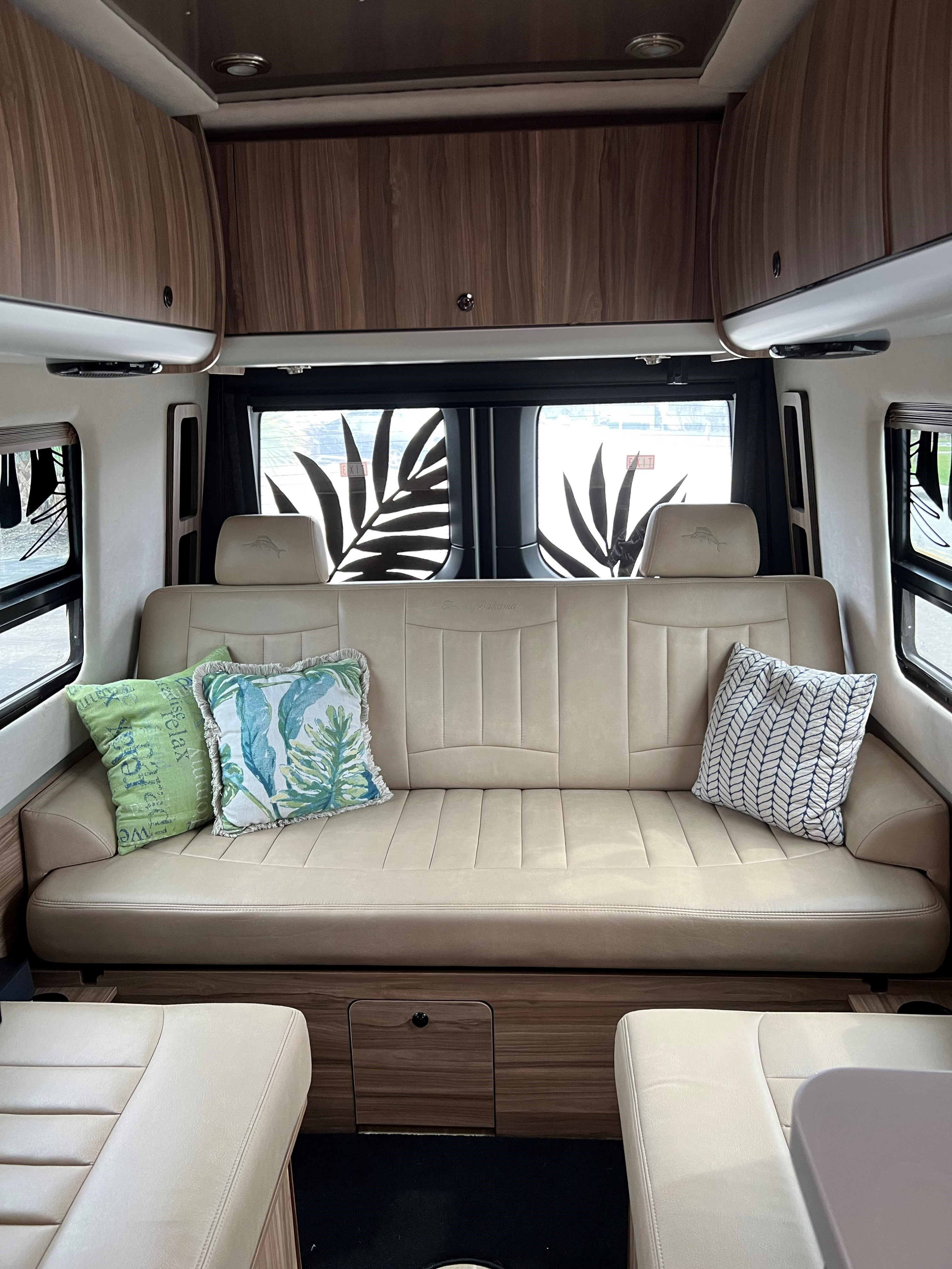 Step inside a clean, modern RV rental. Beige leatherette sofa/bed, wood overheads, and palm leaf window art.. Airstream Interstate 2021