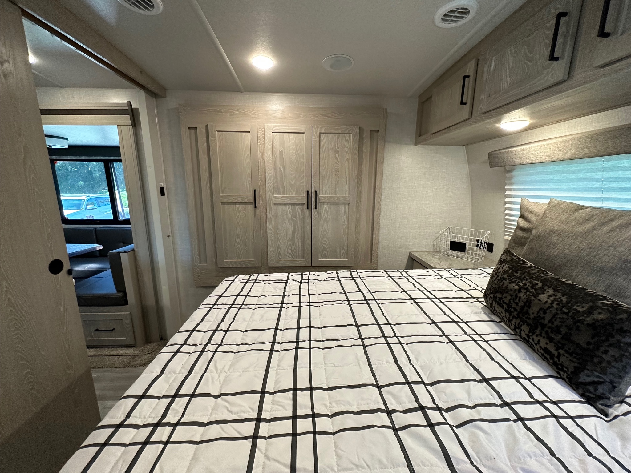 Cozy RV rental bedroom with modern plaid bedding, wooden cabinets, and a view into the dinette area.. Forest River Rockwood Ultra Lite 2021