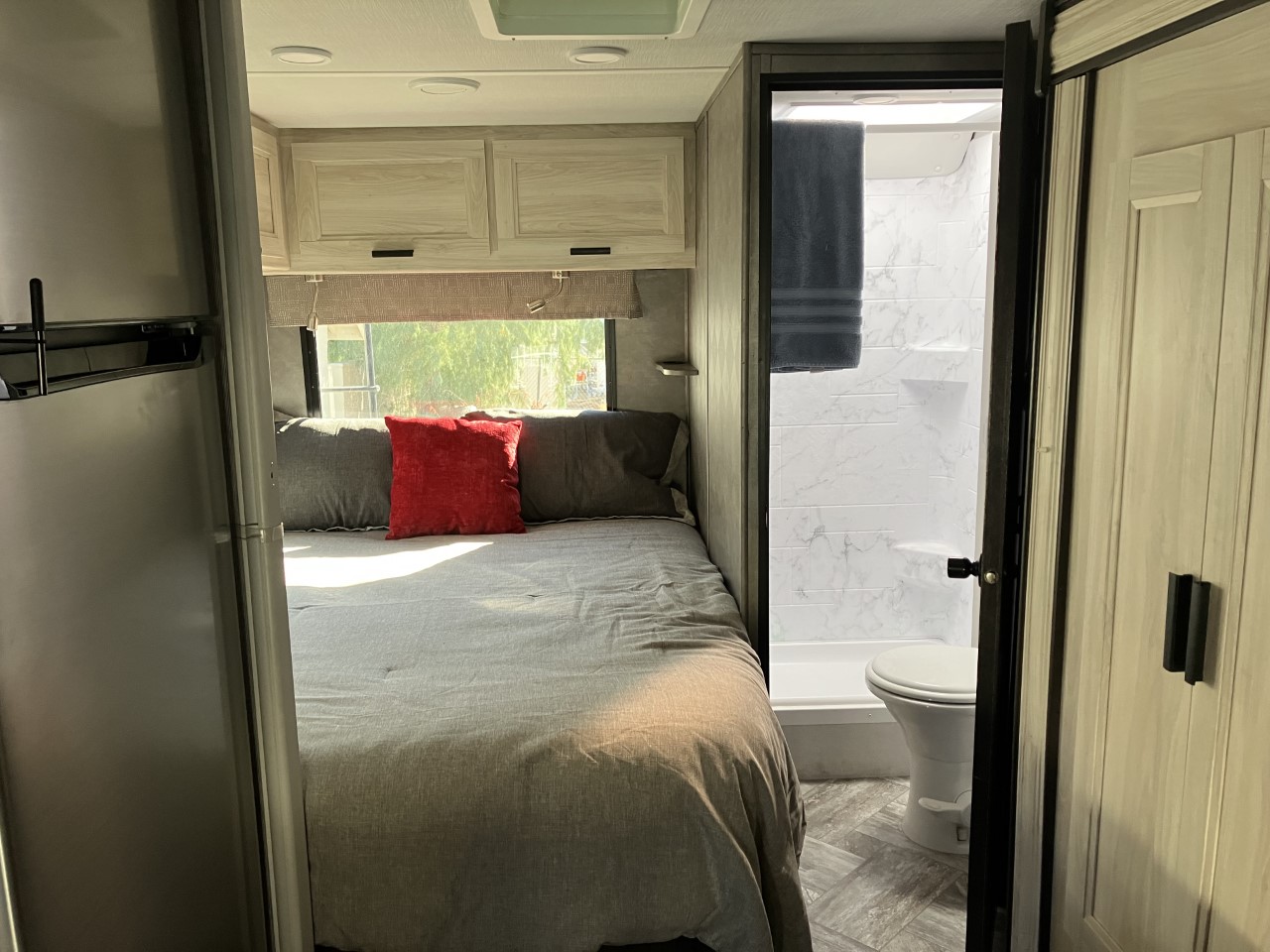 RV rental interior: cozy bedroom with a large bed, window, cabinets, and an adjacent compact bathroom with shower and toilet.. Forest River Sunseeker LE 2022