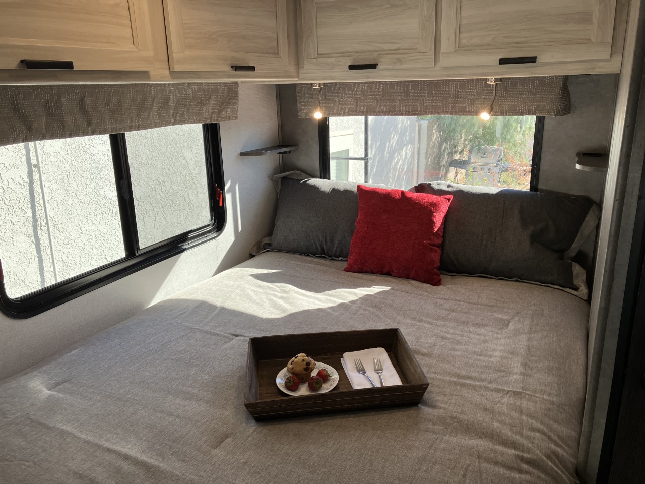 Comfortable RV rental bedroom featuring a grey bed, red pillow, and breakfast tray with muffin & strawberries. Sunny and inviting.. Forest River Sunseeker LE 2022