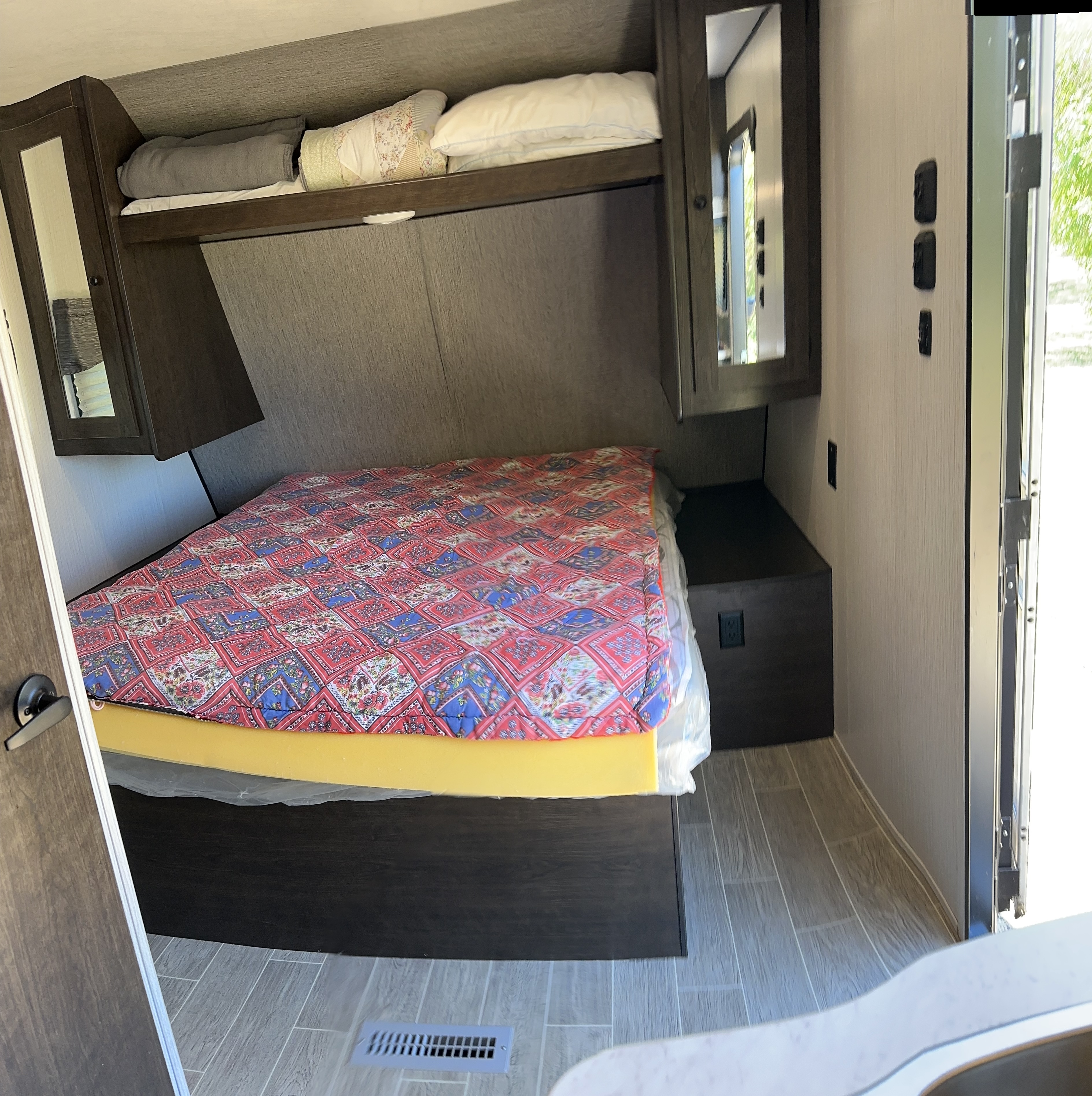 RV rental bedroom interior, showing a compact bed, overhead storage, and a light-colored wall with controls.. Heartland RVs Trail Runner 2020