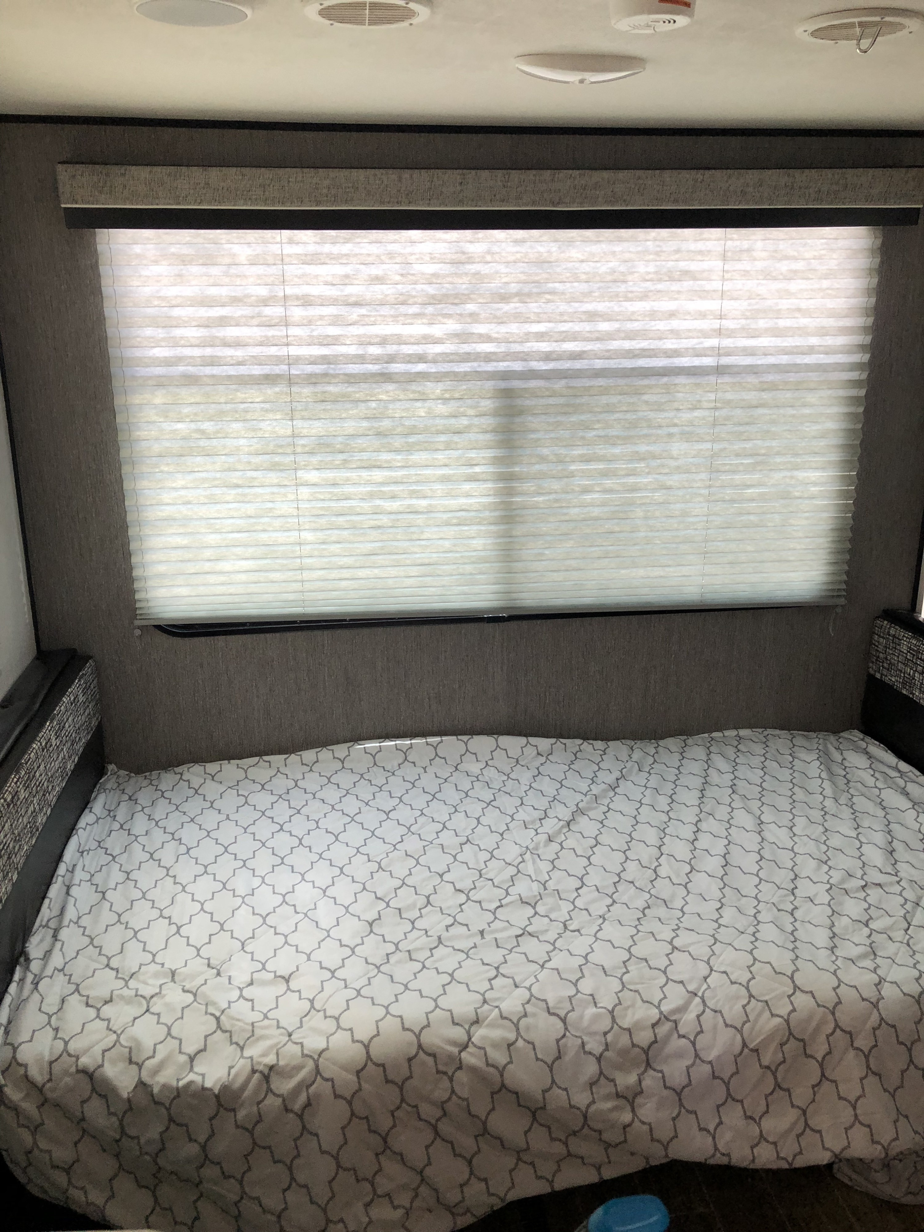 A cozy RV rental interior features a bed with a patterned cover, a large window with pleated privacy blinds, and ceiling fixtures.. Heartland RVs Trail Runner 2020
